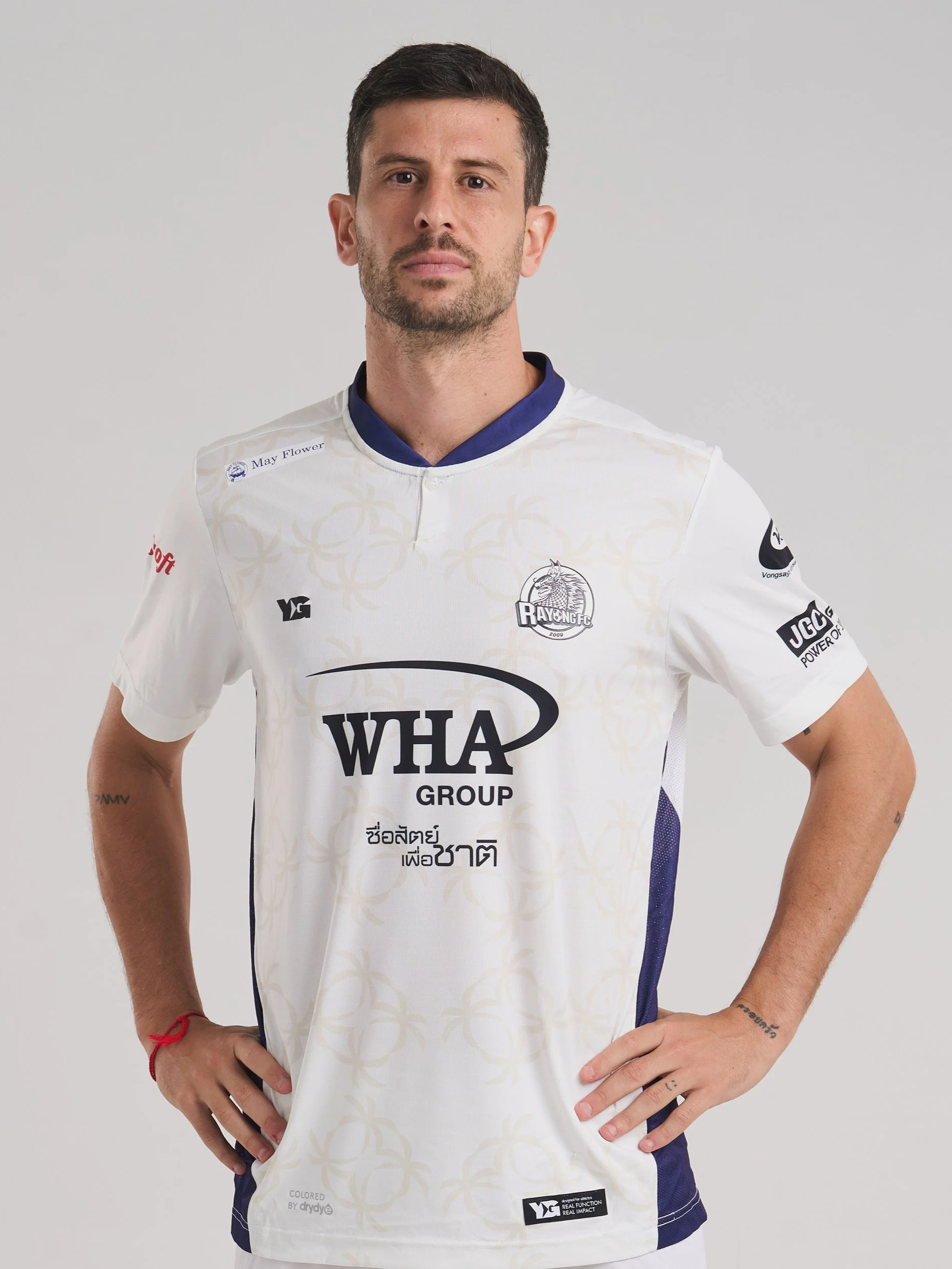 A man wearing a sports jersey with various logos and texts, standing with his hands on his hips against a plain gray background.