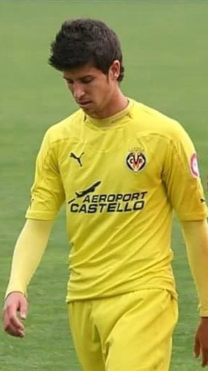 A young male soccer player wearing a yellow Villarreal FC jersey on the field, looking down.