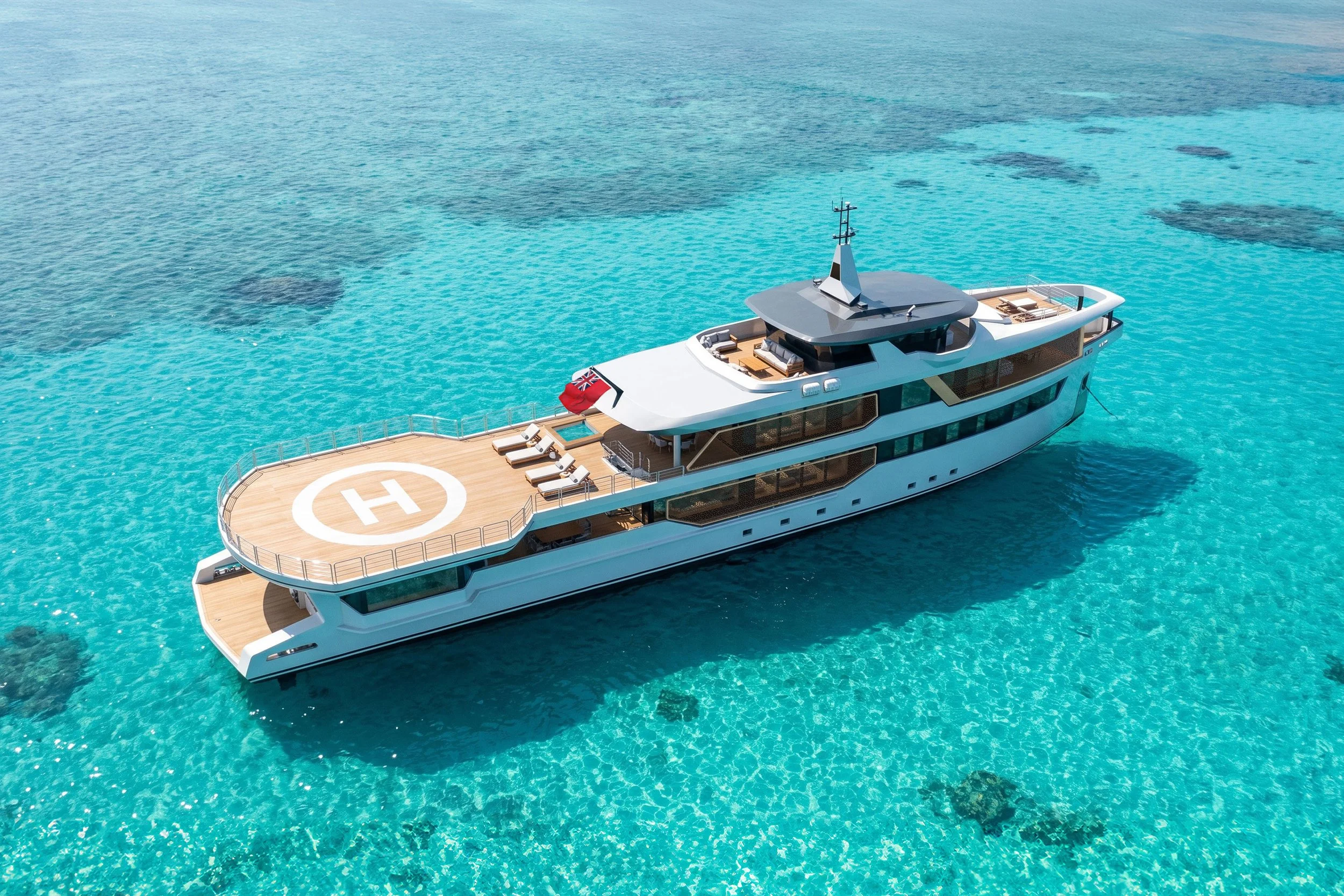 A luxury yacht with a helipad on the deck is floating on clear turquoise water.