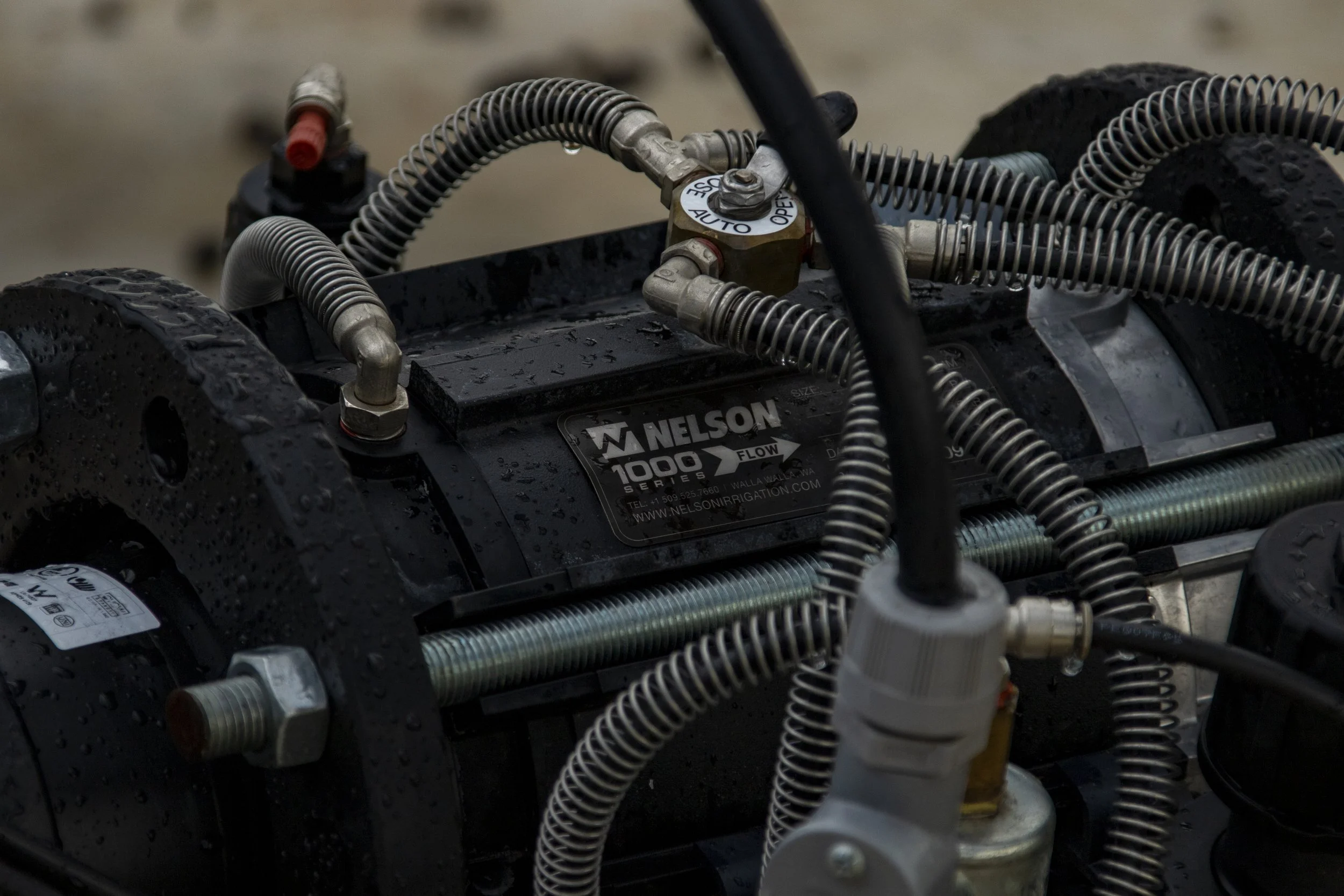 Close-up of a black Nelson 1000 series irrigation pump with metal pipes and hoses attached, some with water droplets, on a wet surface.