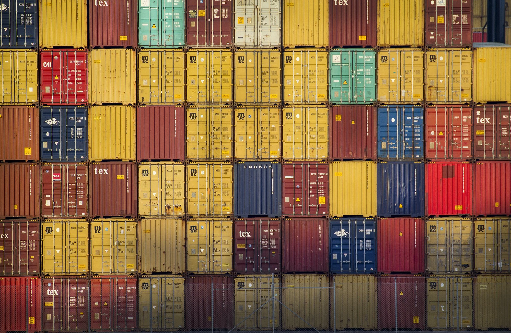 Stacks of multicolored shipping containers arranged in rows at a port.