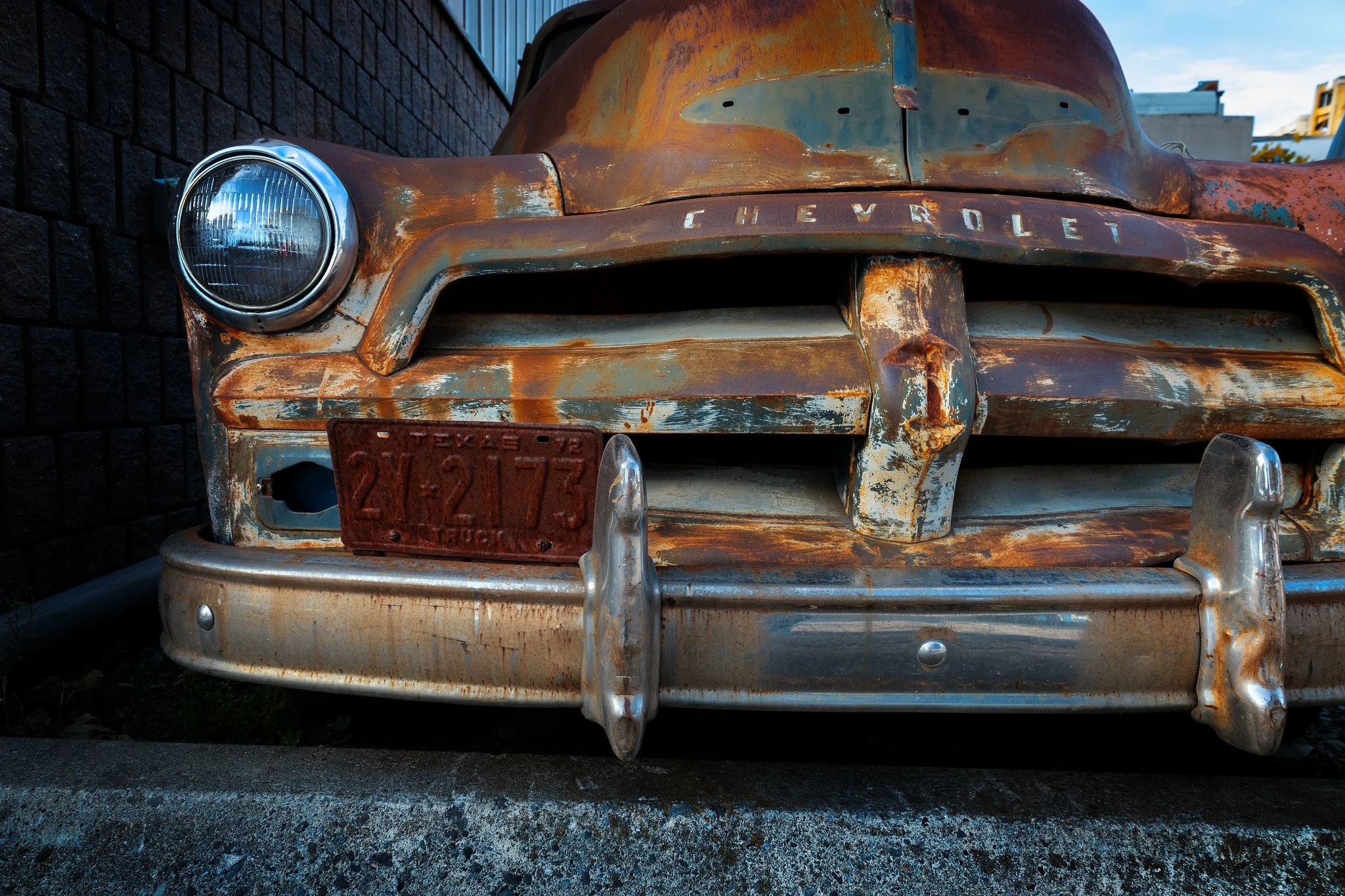 Close-up of an old, rusty Chevrolet truck with a weathered front grille and bumper, showing a Texas license plate reading 2Y-2173.