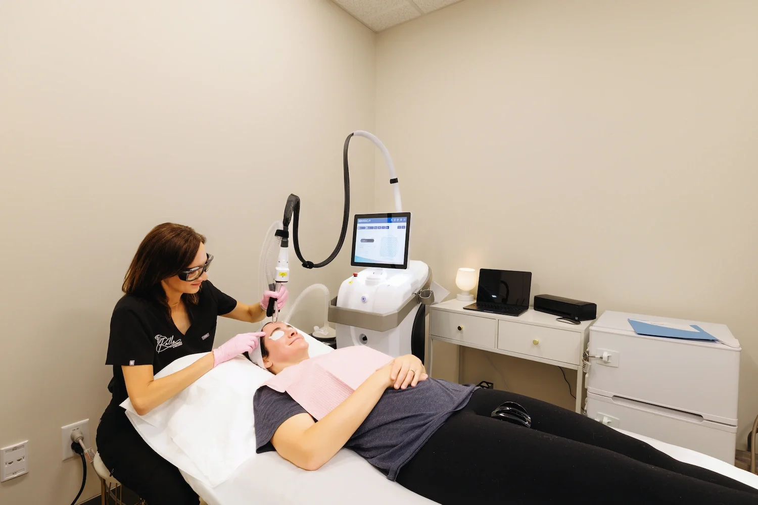 Provider performing facial laser treatment on reclining patient in modern med spa room