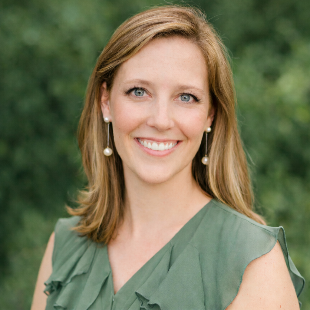 Speech therapist with shoulder-length light brown hair, wearing earrings with pearl drops and a sleeveless green top, smiling outdoors with greenery in the background.