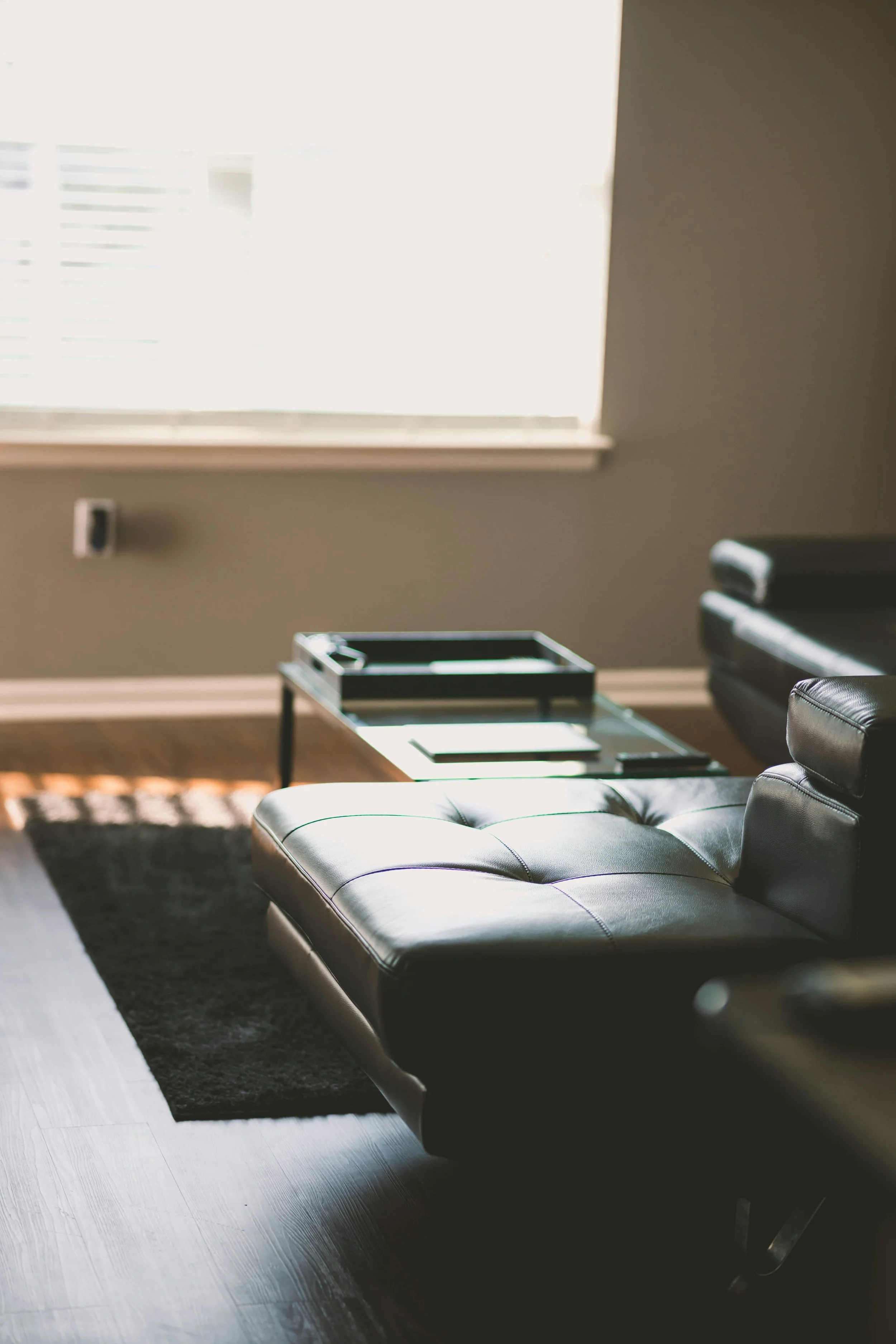 A modern black leather chaise lounge in a room with a window and a small coffee table with magazines.