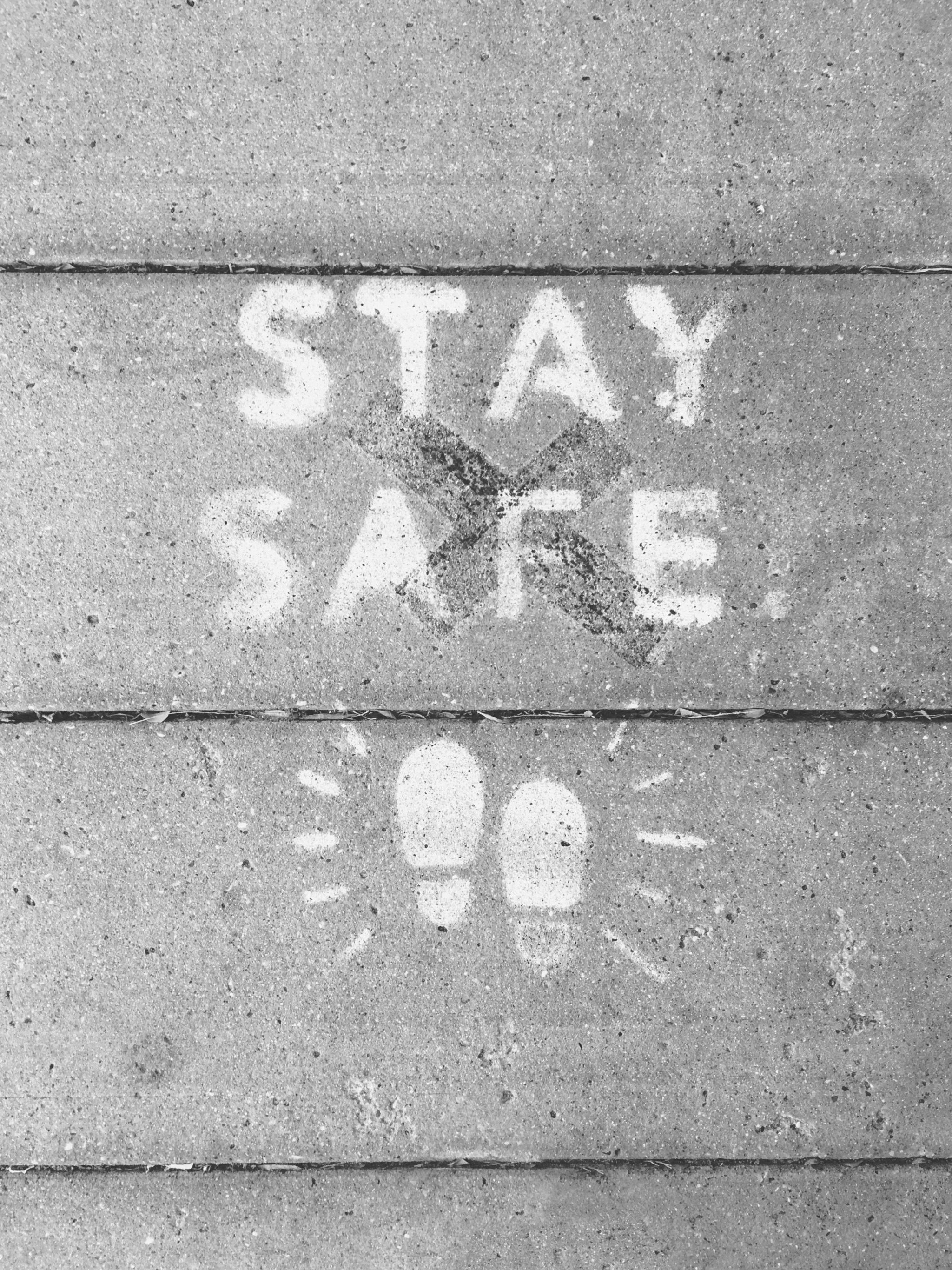 A sidewalk with the words "STAY SAFE" spray painted on it in white letters.