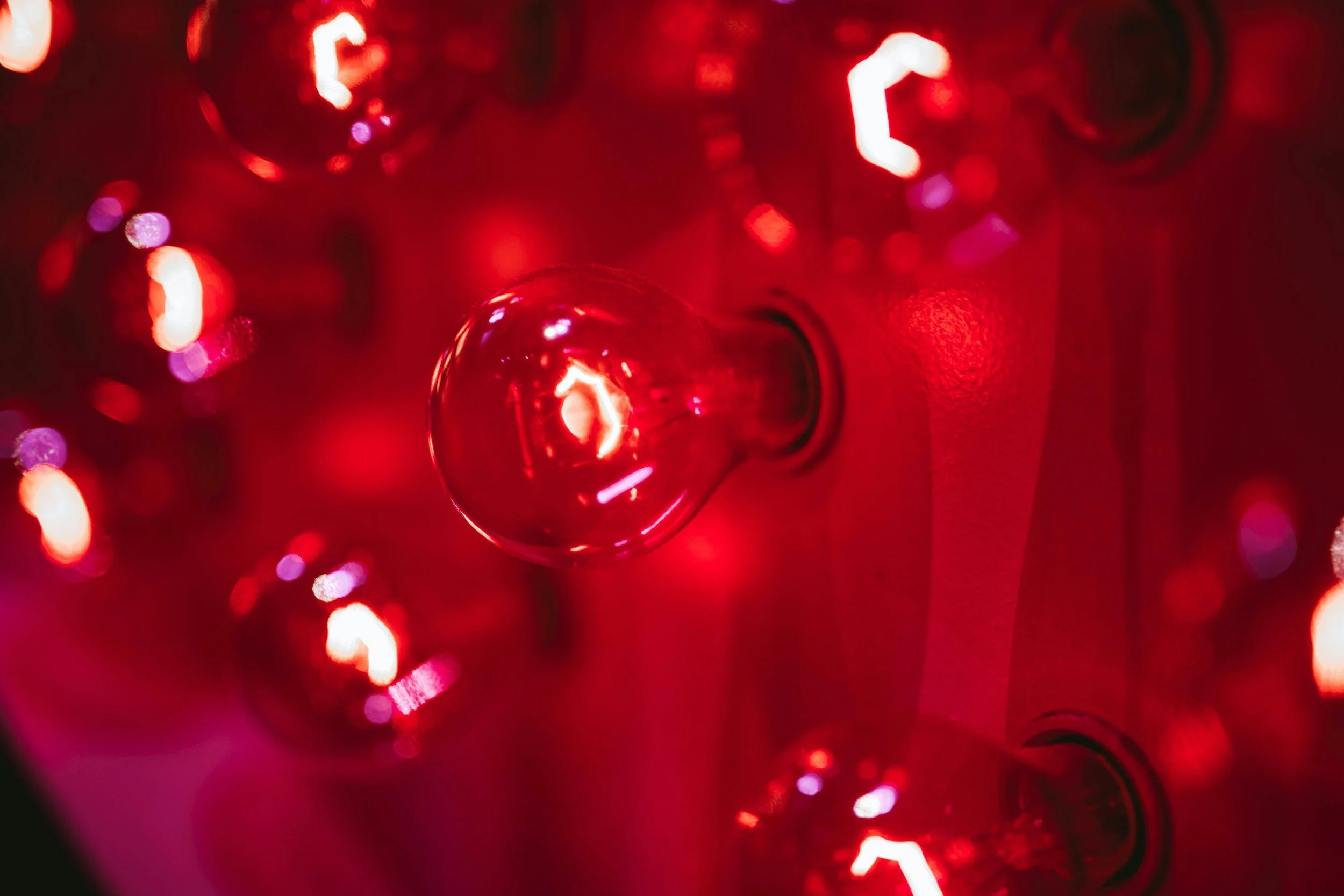 Close-up of red Christmas lights creating a bokeh effect with a shiny red ornament in the center.