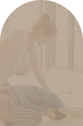 A woman sitting on the floor stretching near a large window in a bright room.