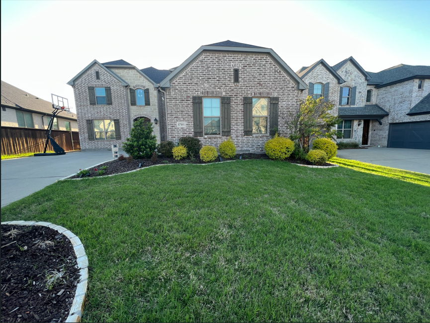Front view of a large brick house with a well-maintained lawn and landscaped bushes, with a basketball hoop on the driveway.