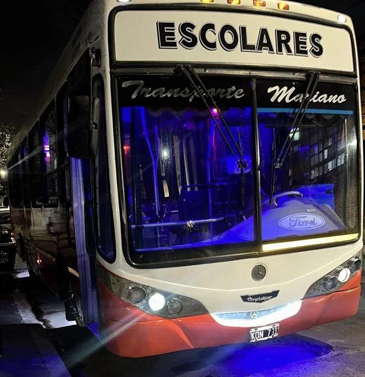 Autobús escolar con luces azules y señal en la parte superior que dice 'Escolares', destino 'Transporte Mariano'.