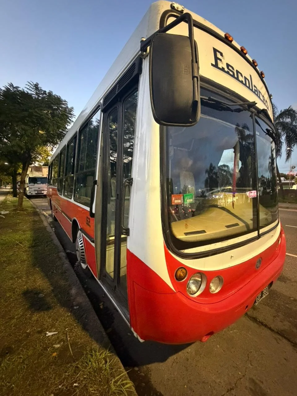 Autobús de color blanco con detalles rojos y negros, estacionado en la calle