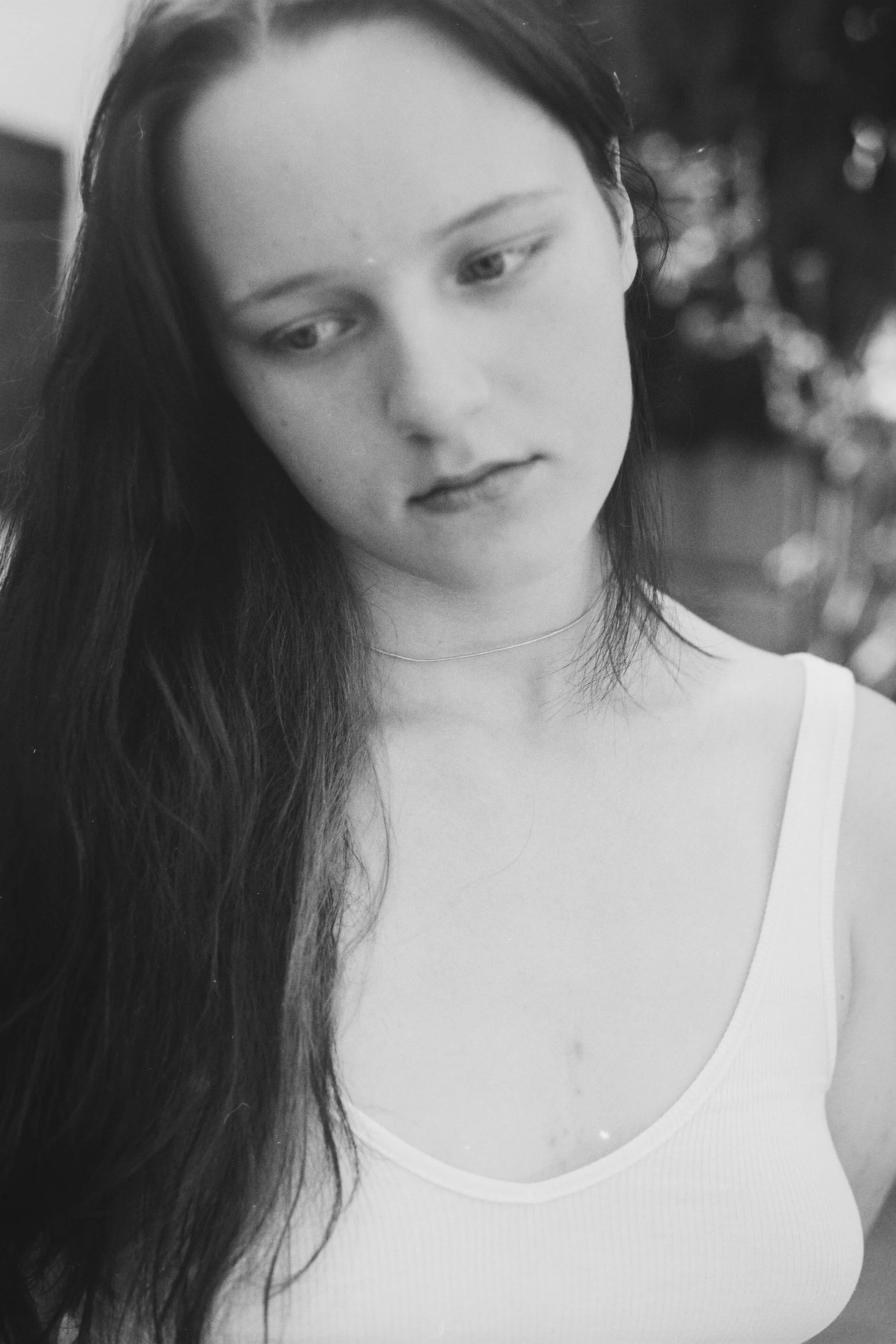 Black and white close-up of a woman with long dark hair wearing a white top, looking down.