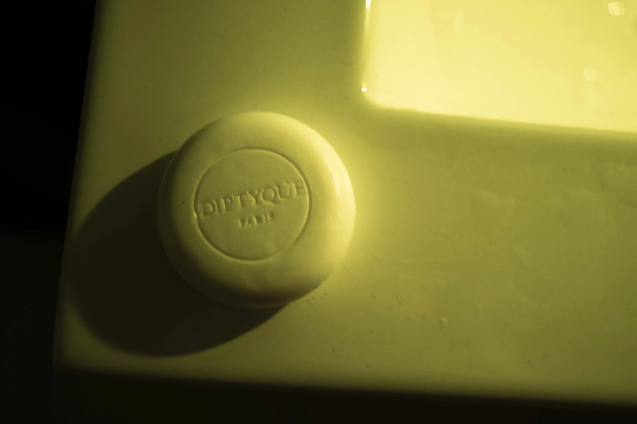 Close-up of a soap with the brand name 'diptych ' embossed on it, on a yellowish sink surface.