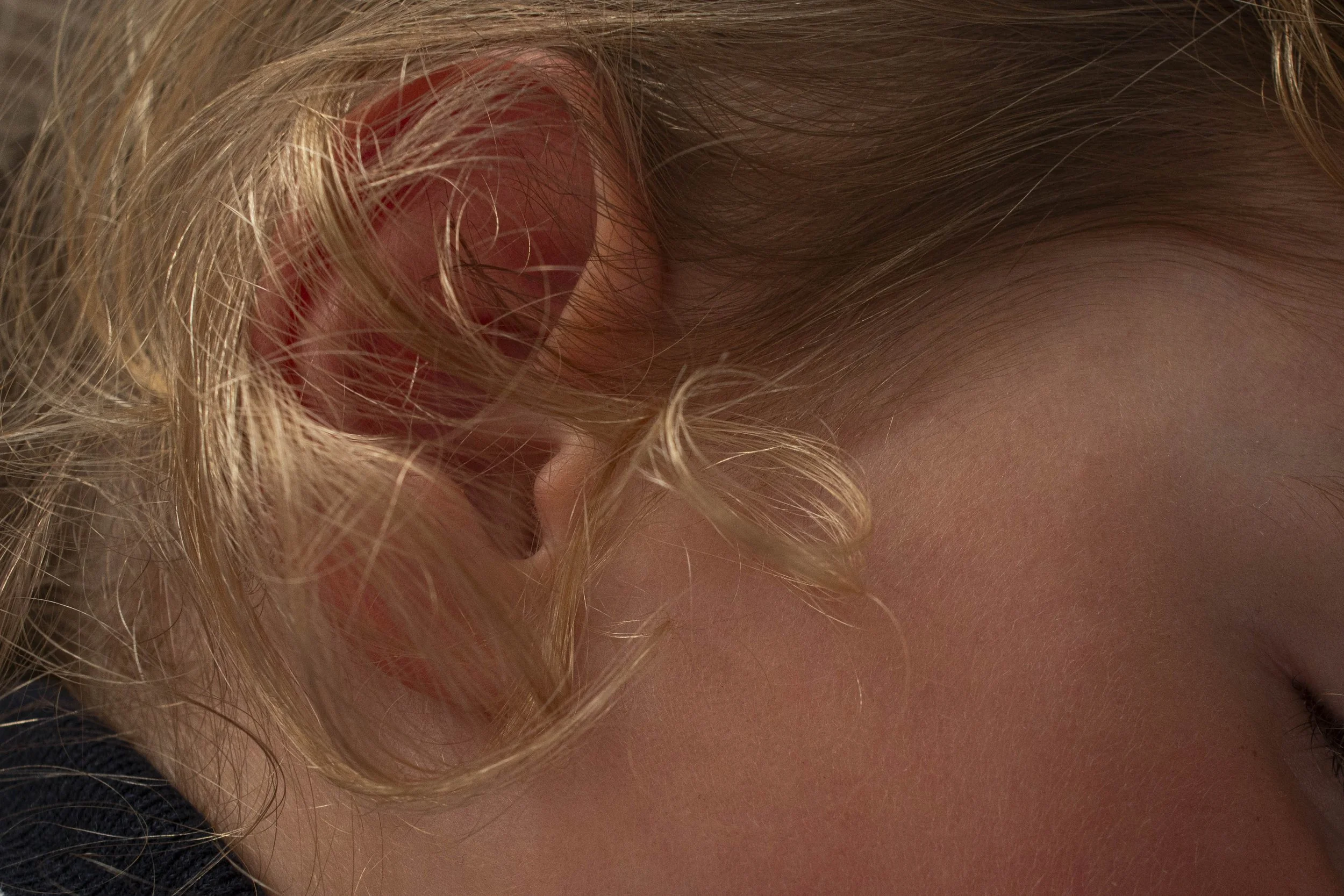 Close-up of a person's ear with blonde curly hair and a portion of their neck.