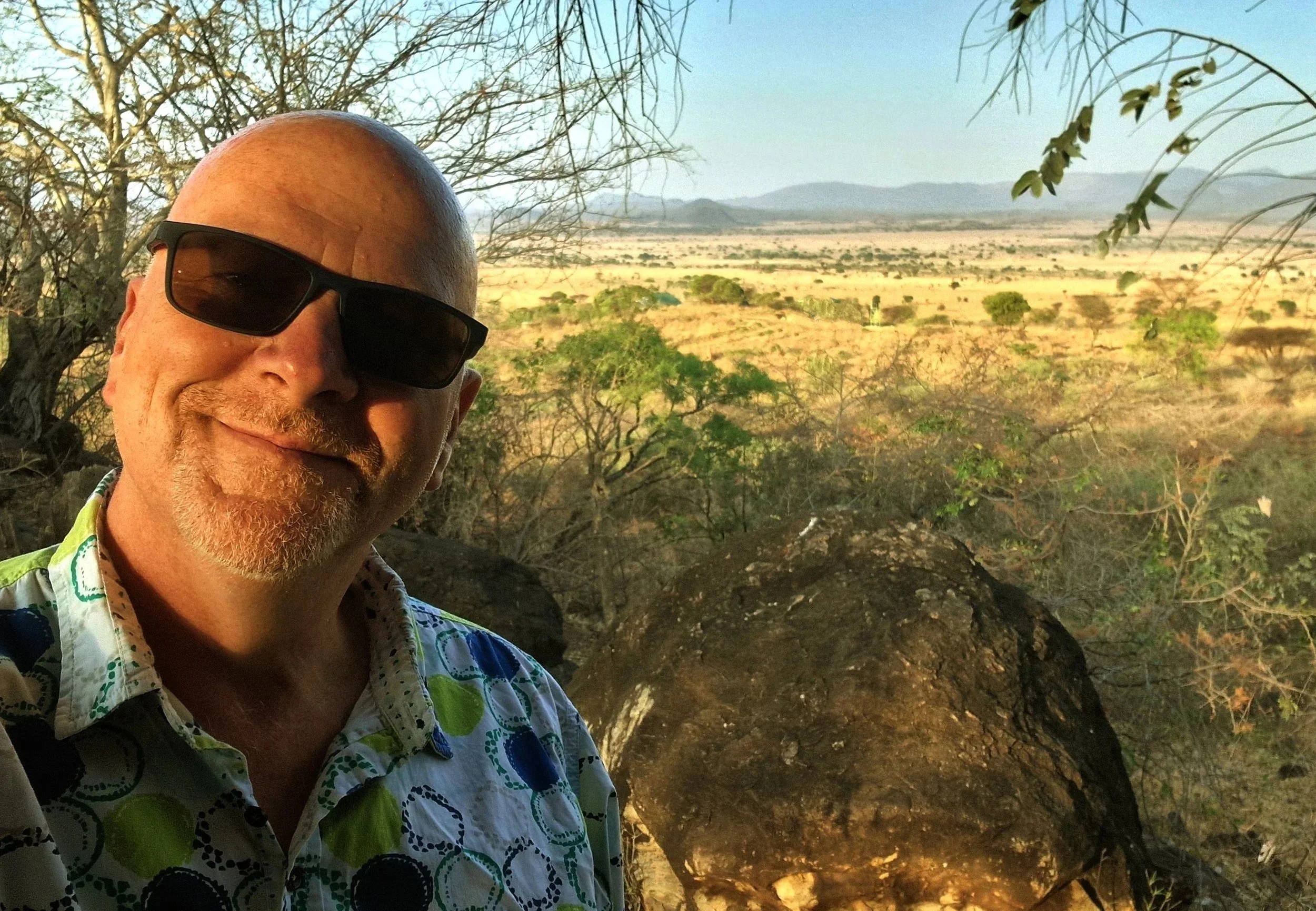 Founder Iain Patton in Uganda an  arid African landscape, sparse trees, and distant mountains in the background.