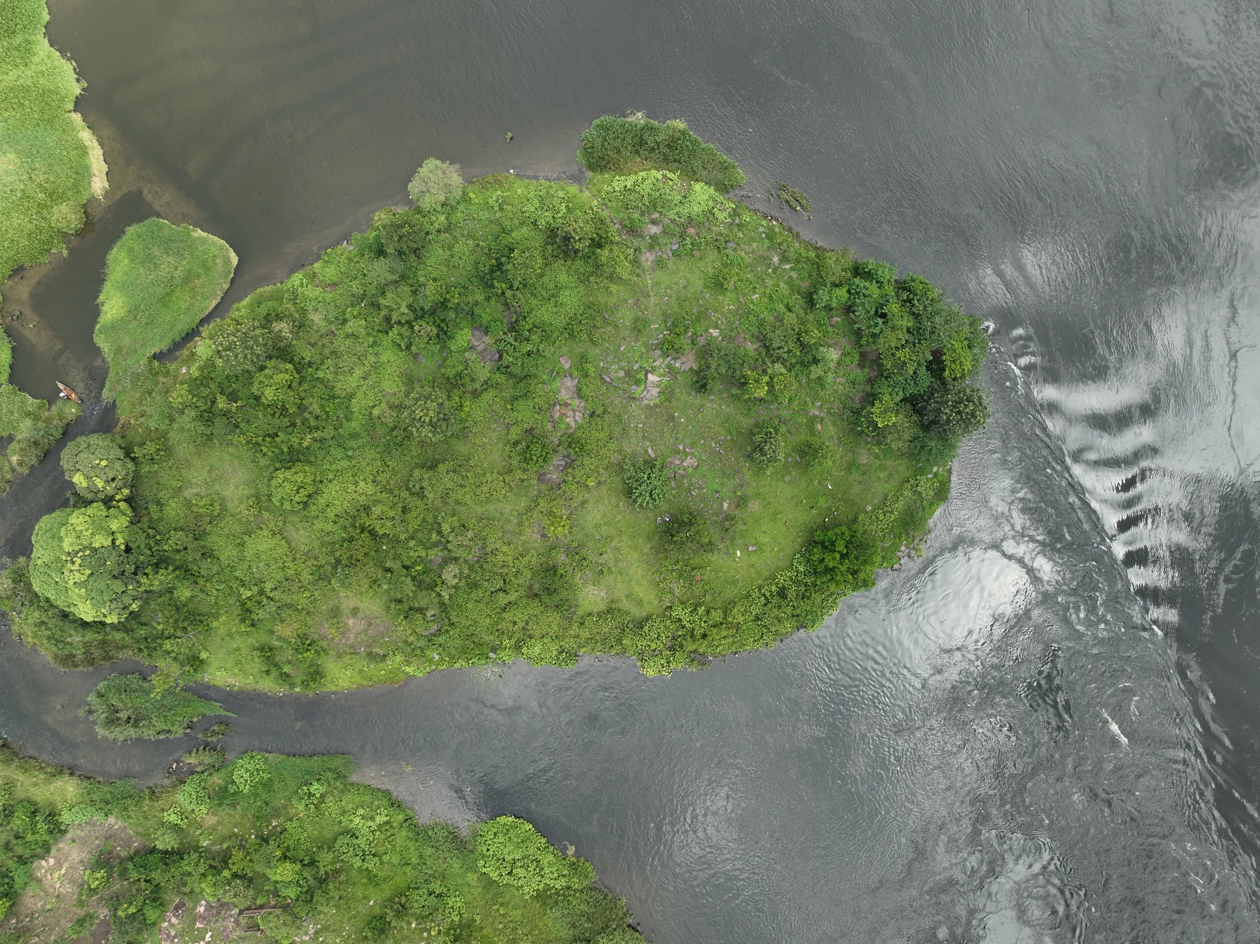 An aerial view of a green forested island surrounded by water, with a small boat near the lower left corner.