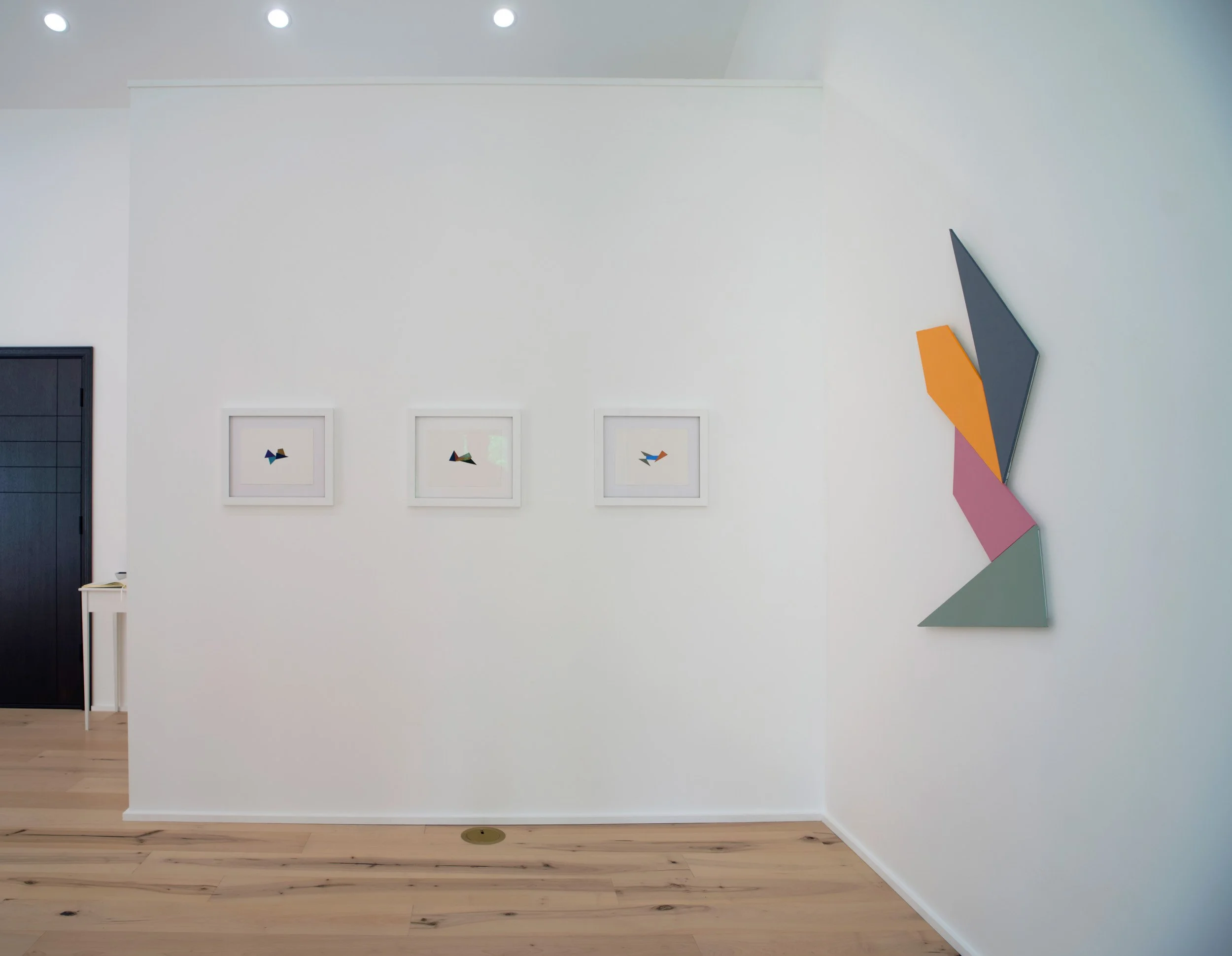 Gallery wall with four abstract framed artworks and a large geometric wall sculpture in neutral and pastel colors in a modern interior.