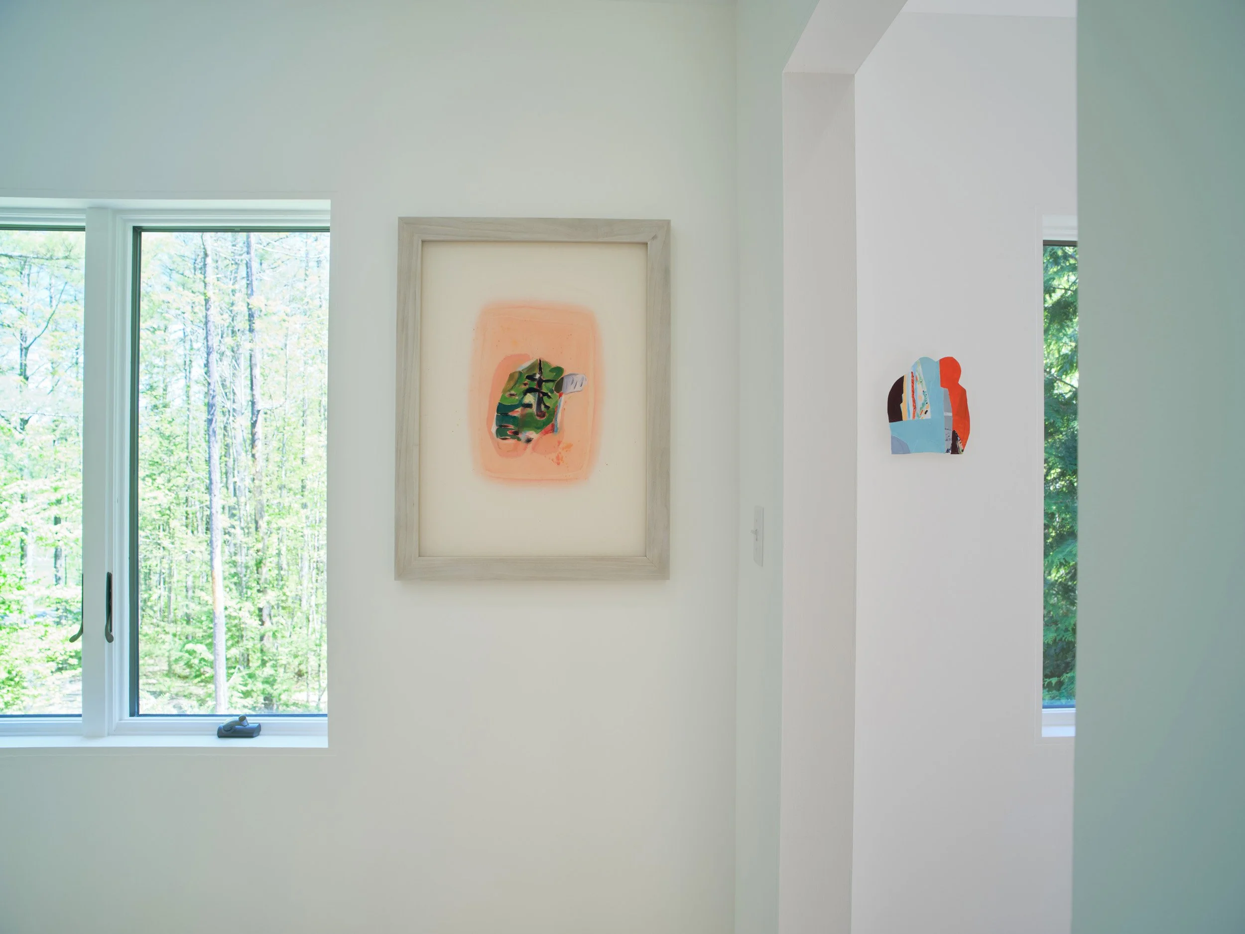 Interior of a modern home with white walls, large windows showing a green outdoor landscape, and abstract artwork hanging on the wall.