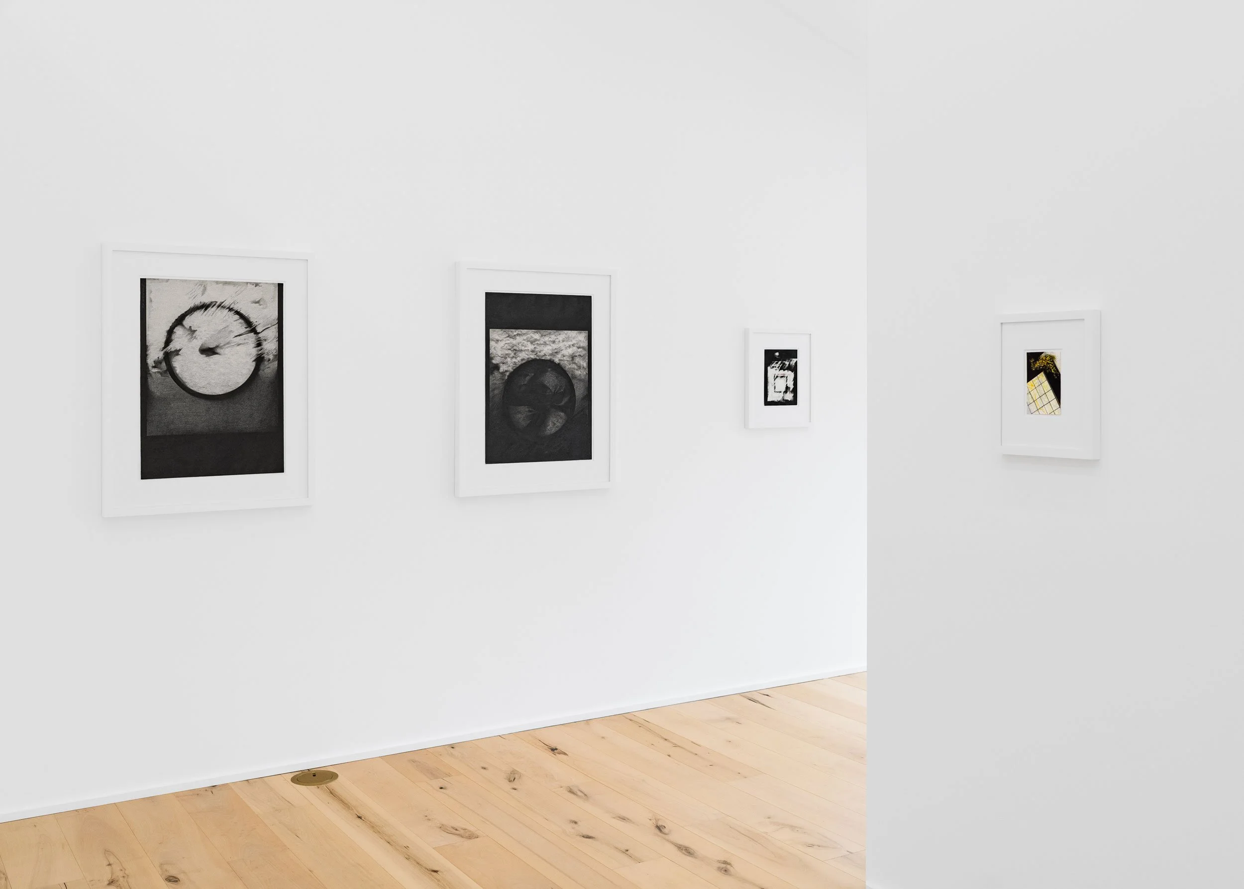 Four framed photographs displayed on a white gallery wall, showcasing abstract black-and-white images, with a light wooden floor beneath.