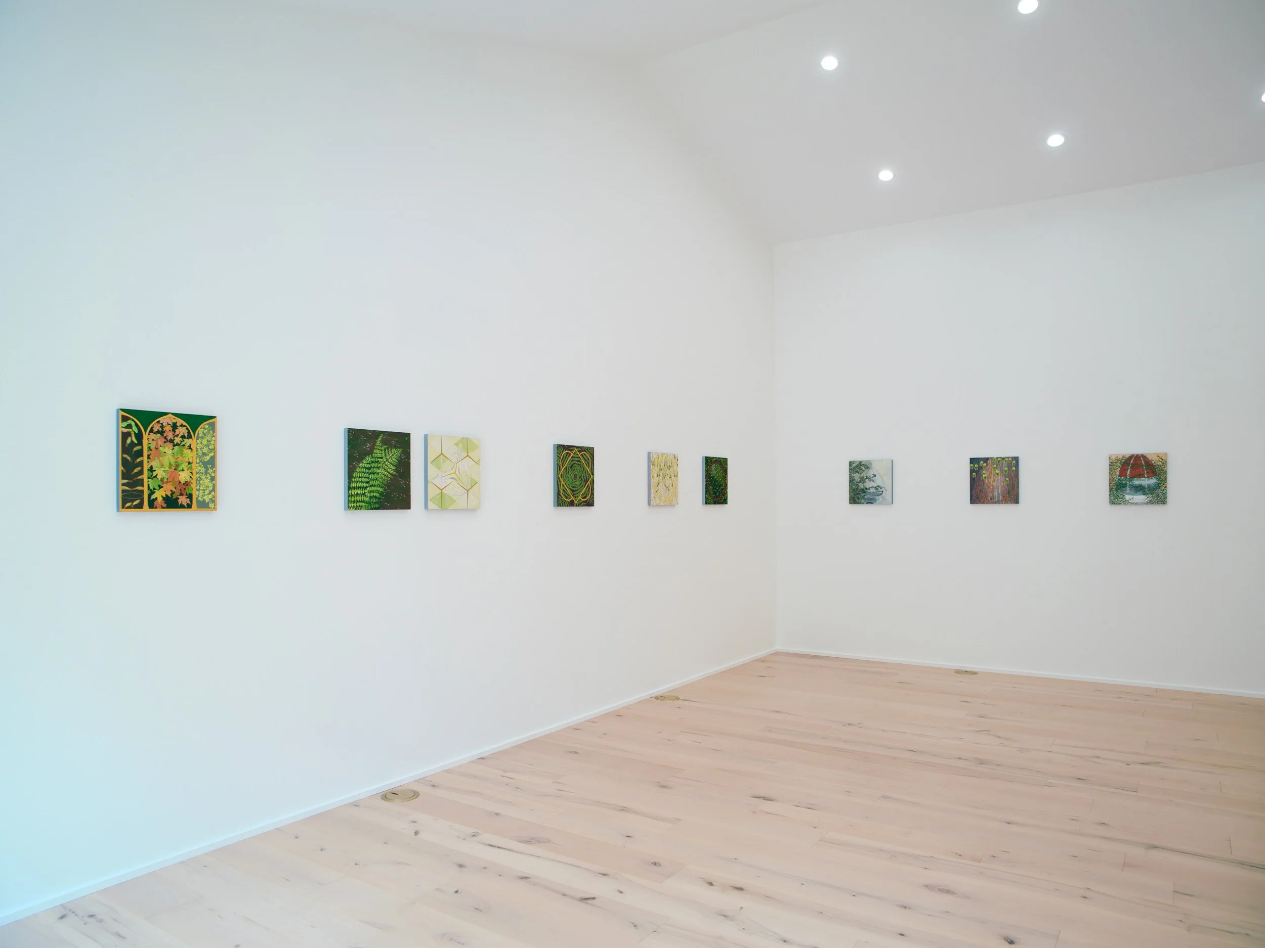 Gallery wall with several small colorful abstract paintings in a white-walled art gallery room.