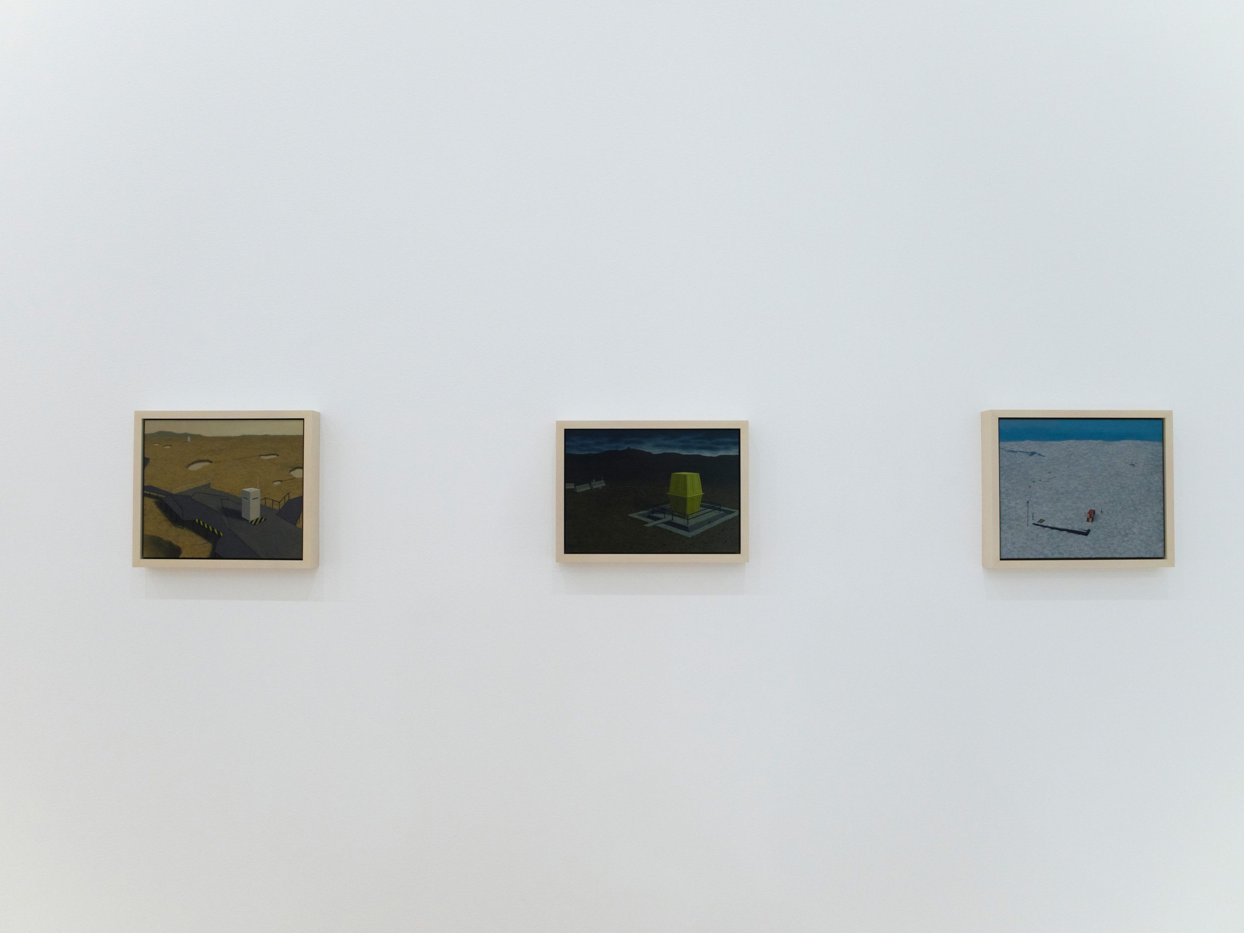 Three framed digital art pieces hanging on a white gallery wall, showing abstract landscapes and structures.