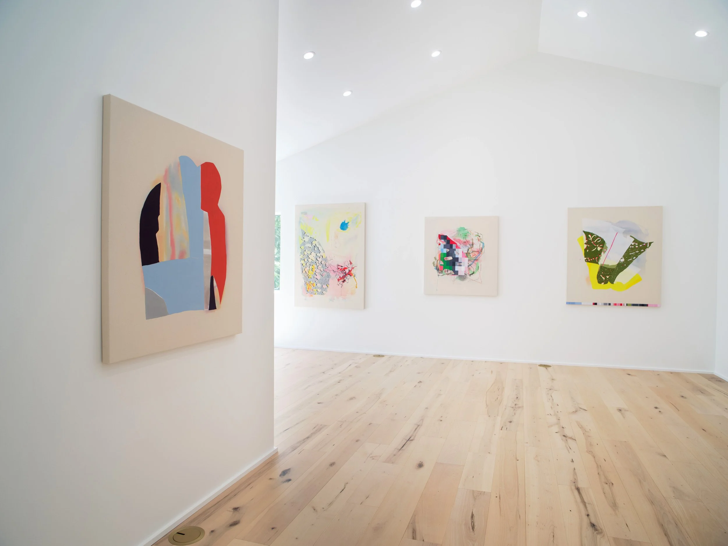 Close-up of an art gallery wall with colorful abstract paintings, white walls, and wooden floor.