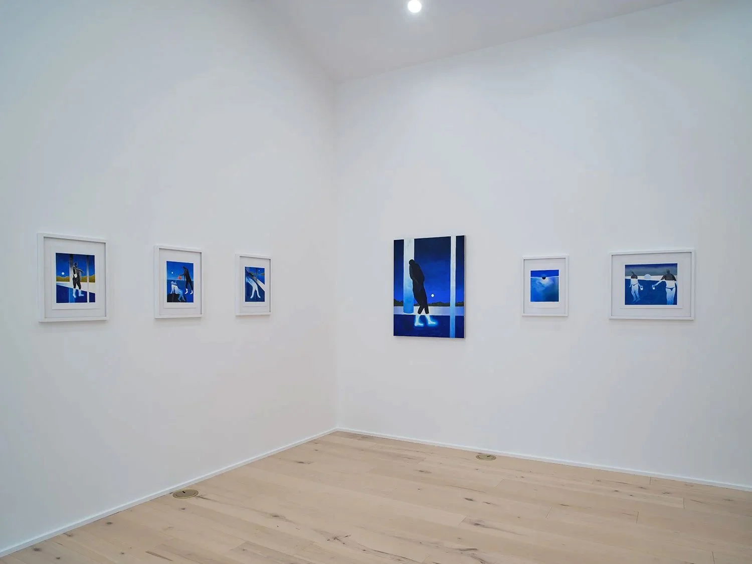 An art gallery with six framed blue-toned paintings on white walls, and a light wooden floor.