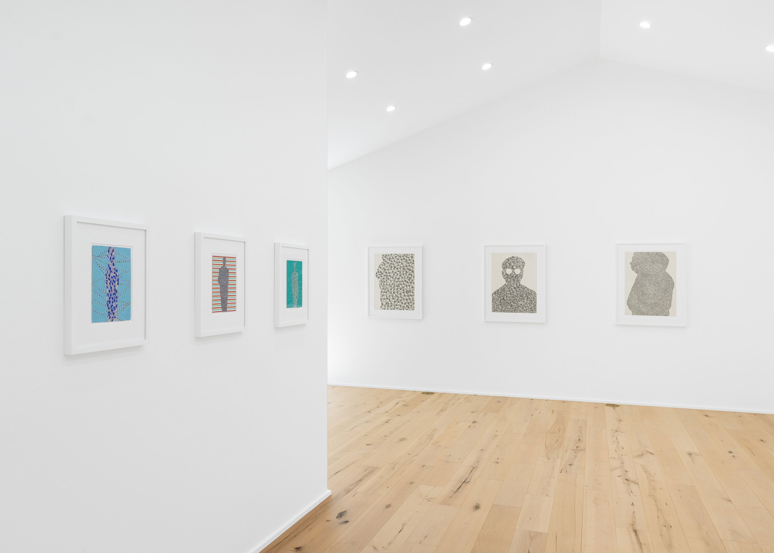 Gallery wall with framed abstract artworks in a minimalist white art gallery with wooden floors and ceiling-mounted lights.