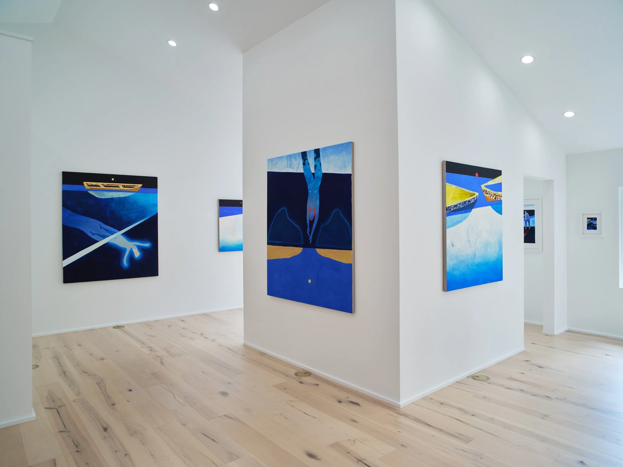 Art gallery with white walls displaying colorful paintings, light wood flooring, and ceiling spotlights.
