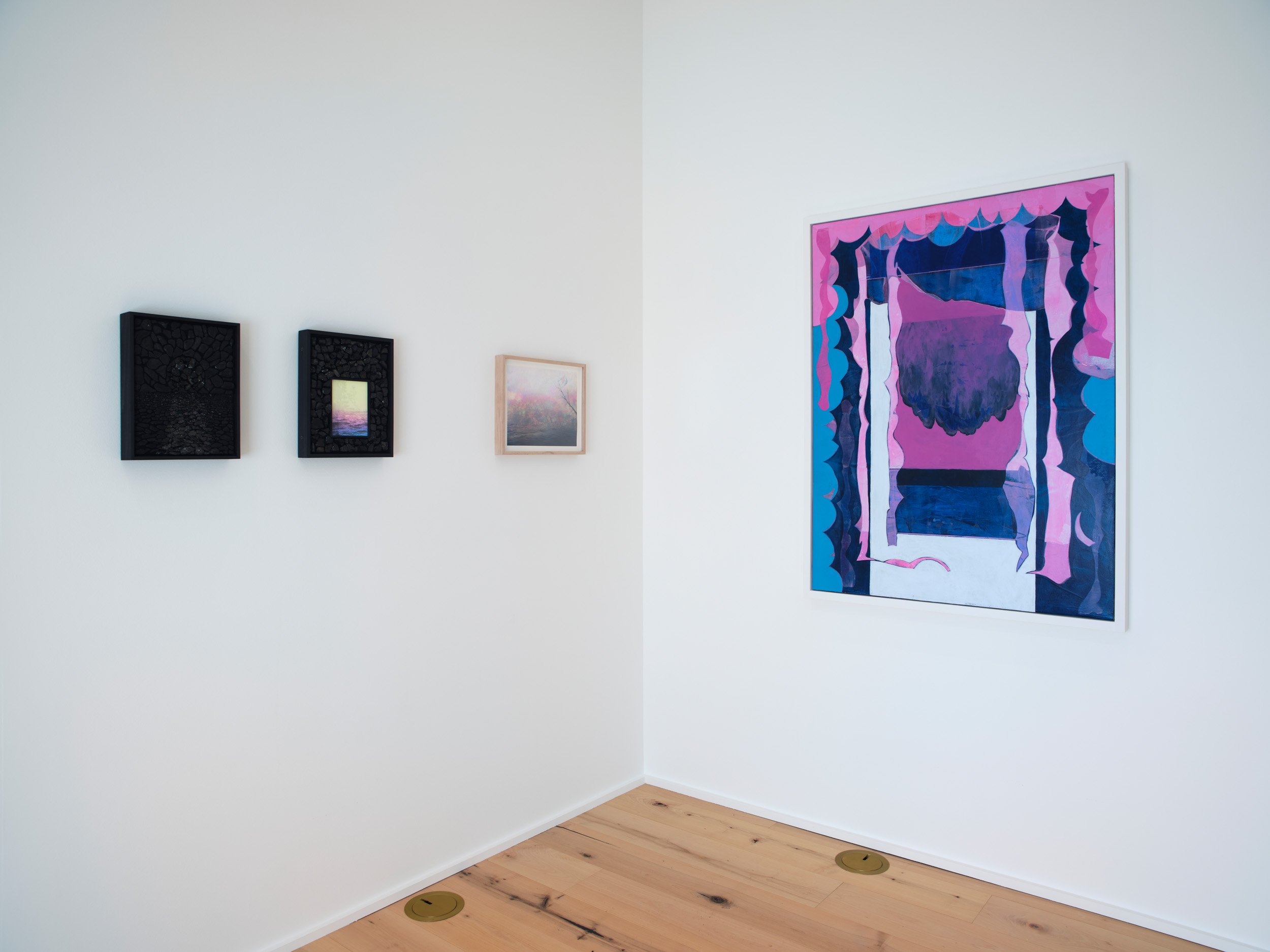 Interior view of an art gallery wall with four framed artworks, two are small, black, textured pieces, one is a small pastel landscape, and one is a large, colorful abstract painting with pink, purple, and blue hues.