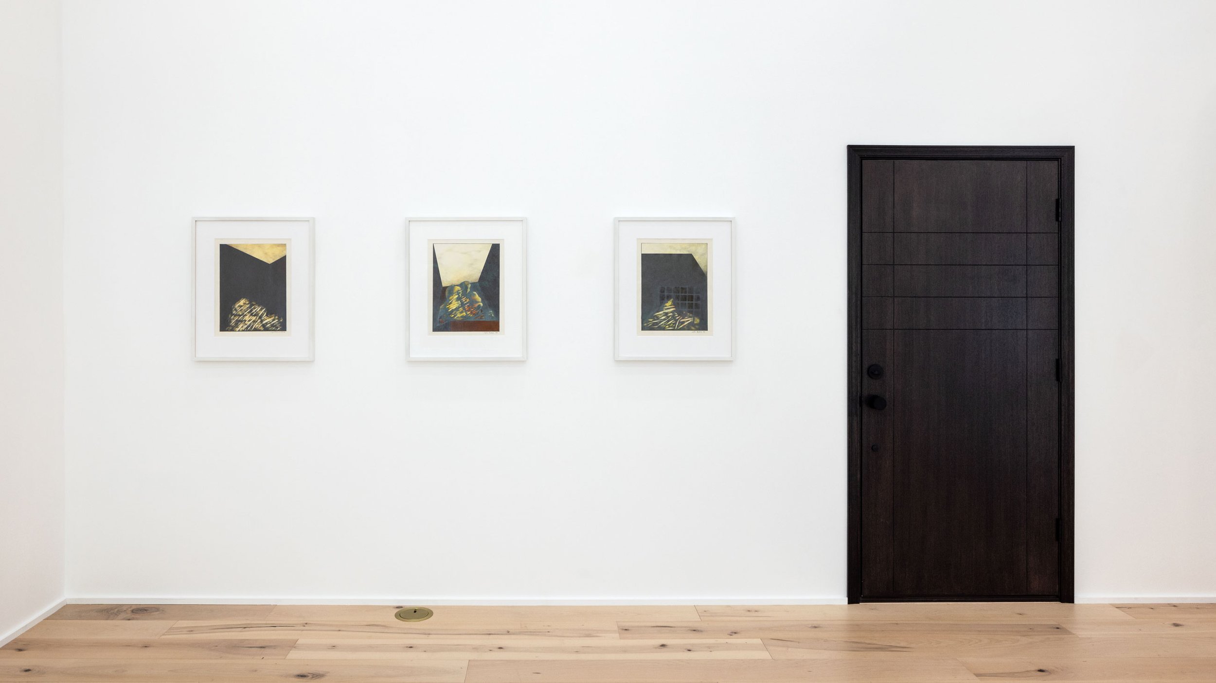 Three framed abstract paintings hang on a white wall next to a dark wood door in an art gallery