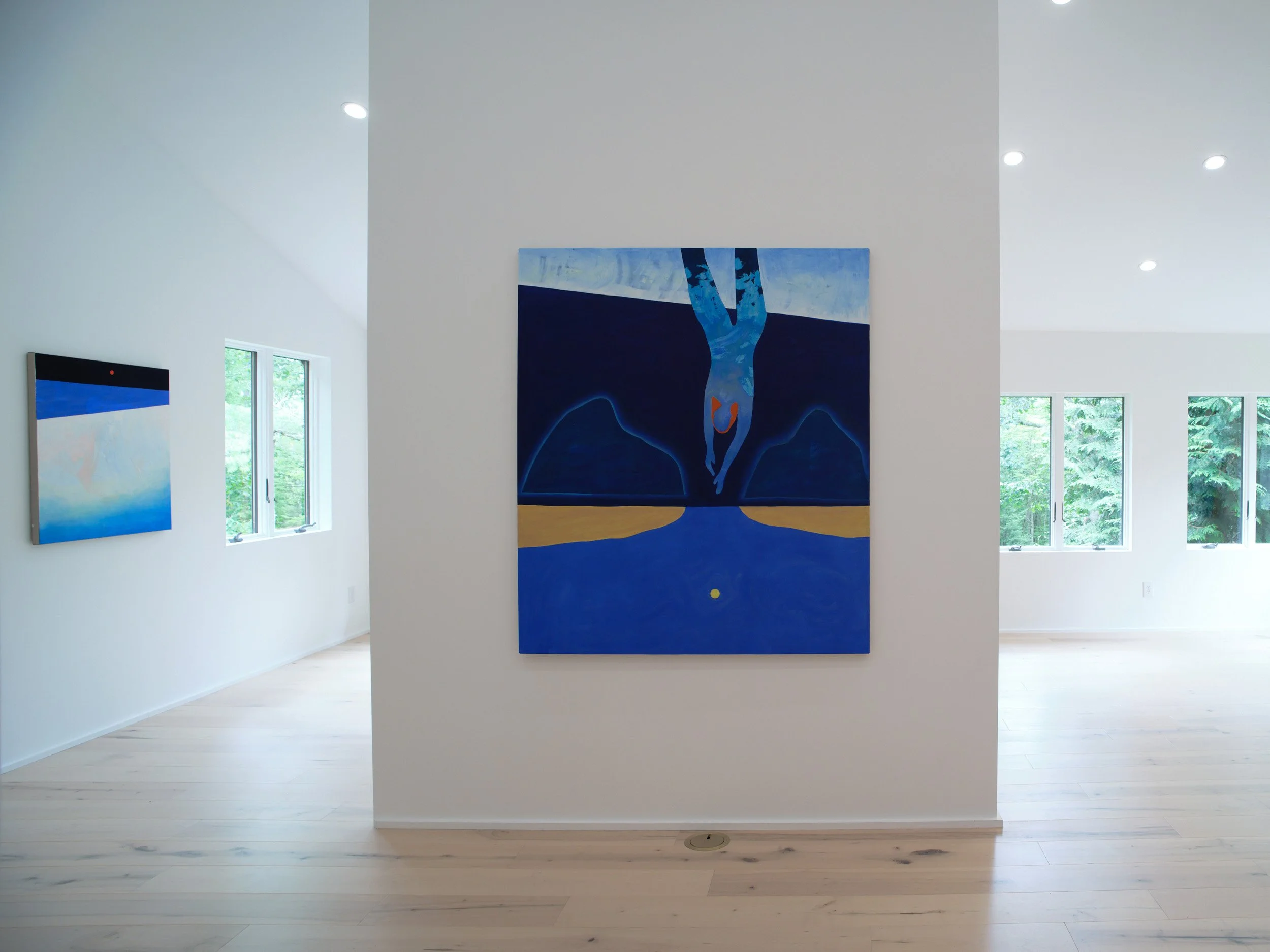 Interior of an art gallery with white walls, natural light coming through windows, and paintings displayed on the walls, including a prominent large blue painting in the center featuring abstract shapes.