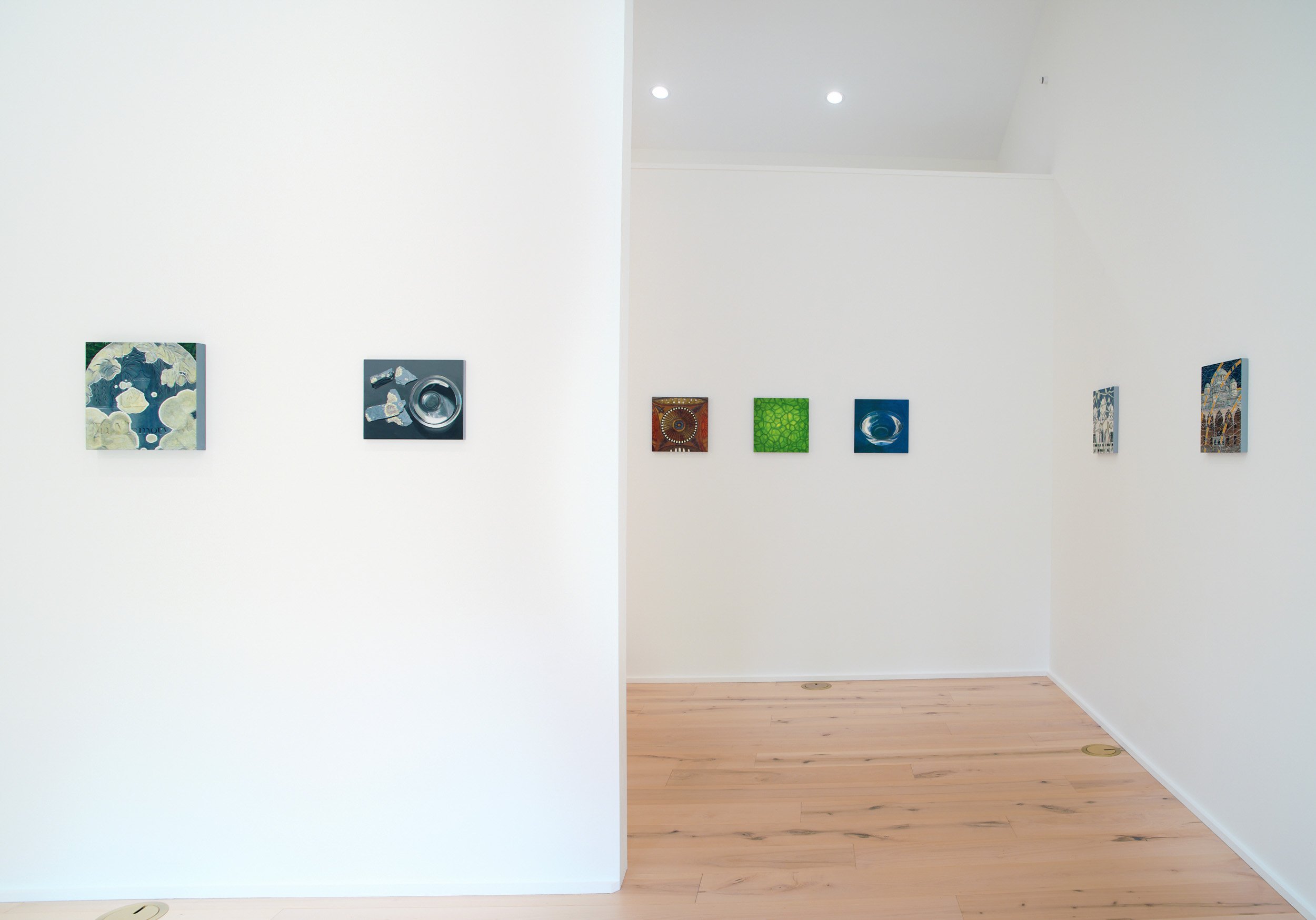 An art gallery with paintings on the wall, white walls, a wooden floor, and ceiling lights.