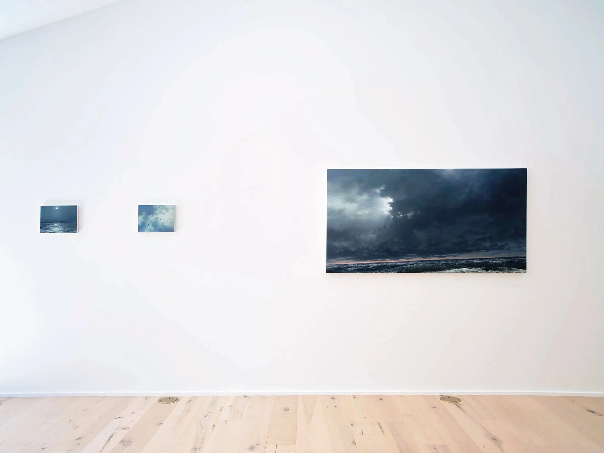 Gallery wall with four landscape photographs of ocean, sky, and stormy clouds on a white wall.