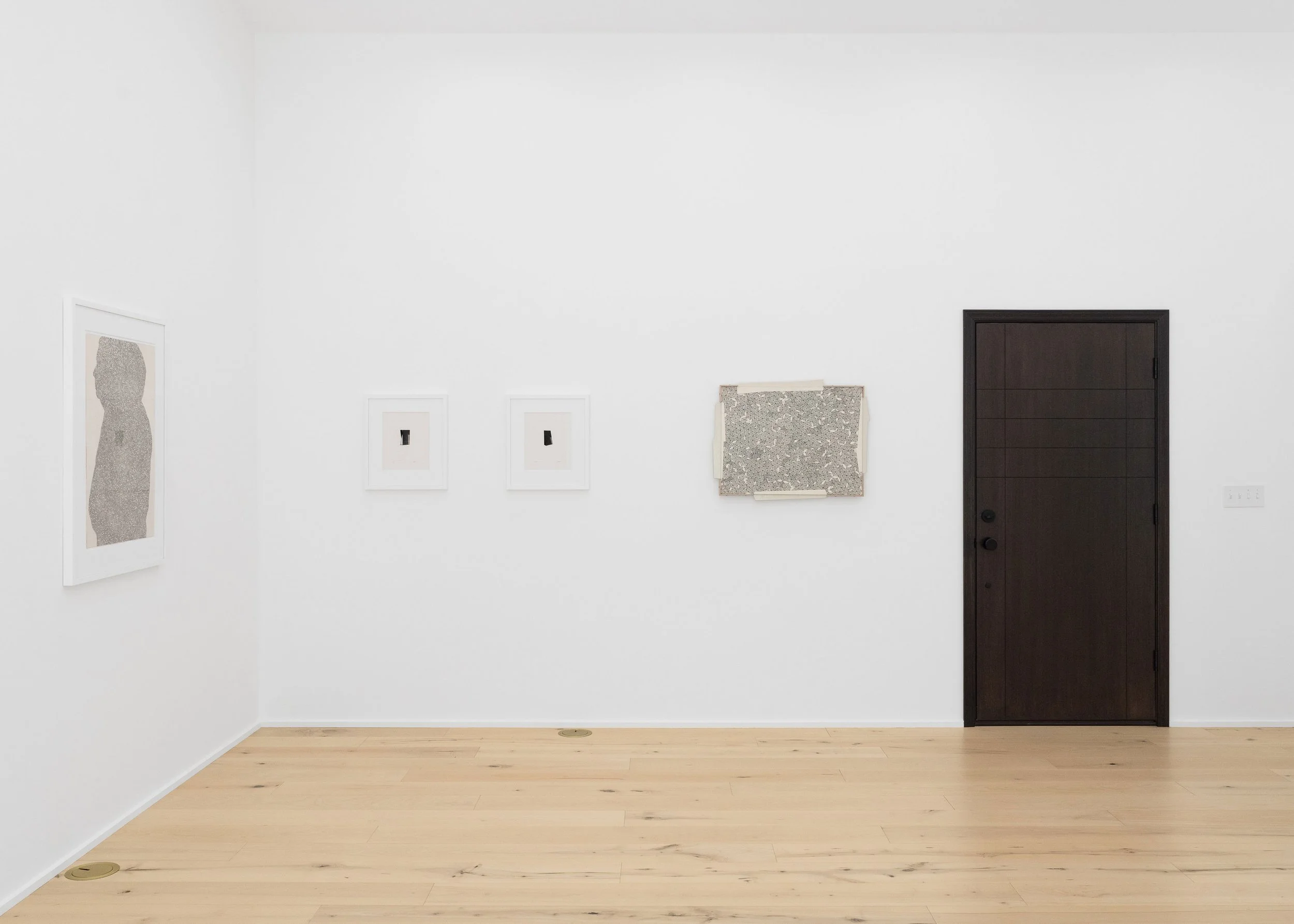 A minimalist art gallery with white walls displaying four pieces, a dark brown door, and light wooden flooring.
