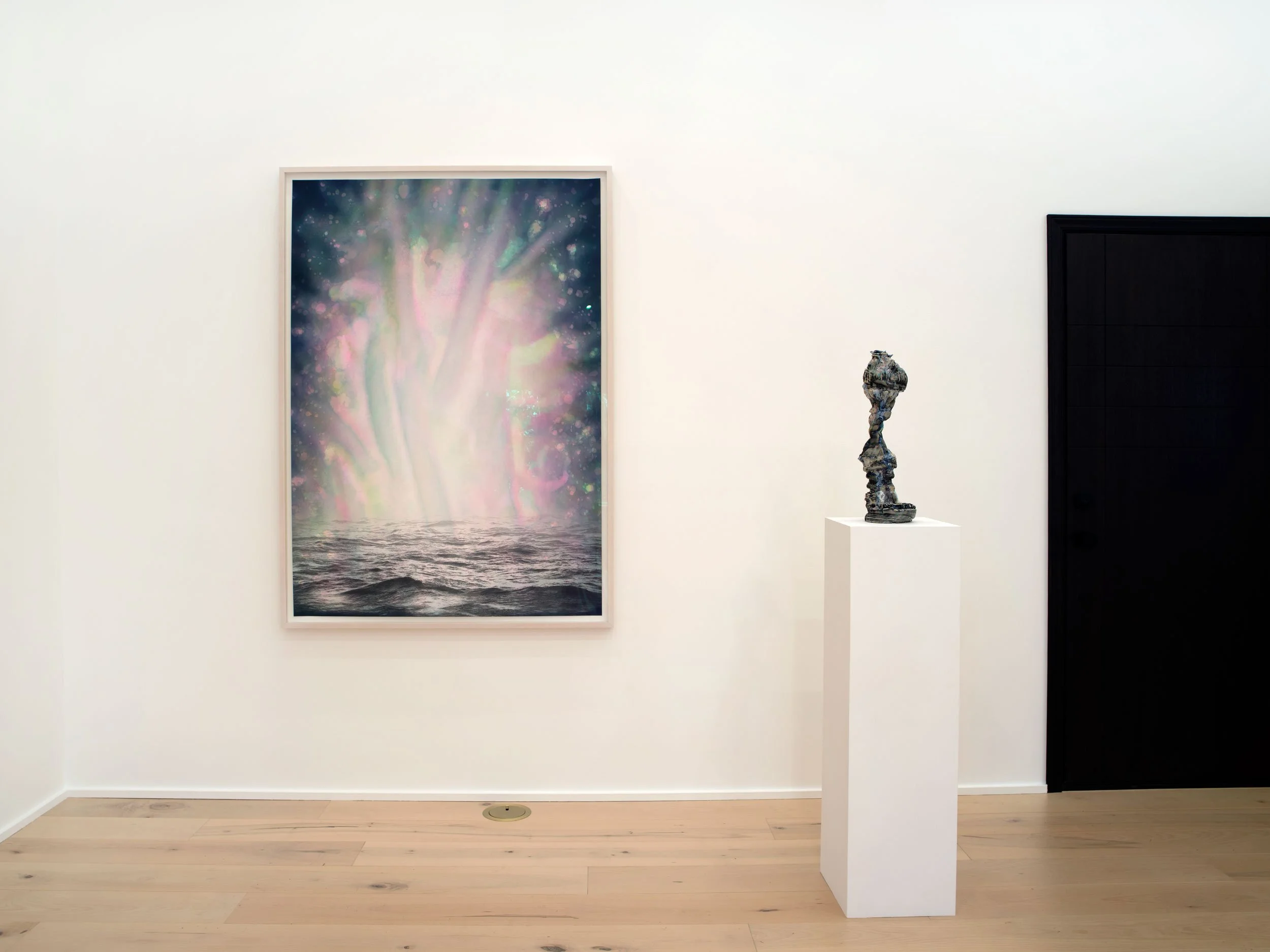 Art gallery with a colorful abstract painting of light reflecting on water, a sculptural piece on a pedestal, and a closed black door in a white-walled room.