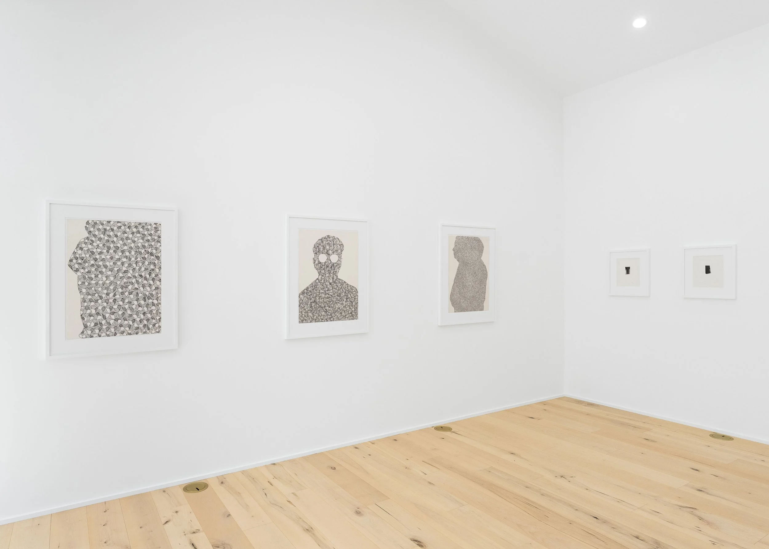 Art gallery with framed artwork on white walls, light wooden floors, and ceiling lights.