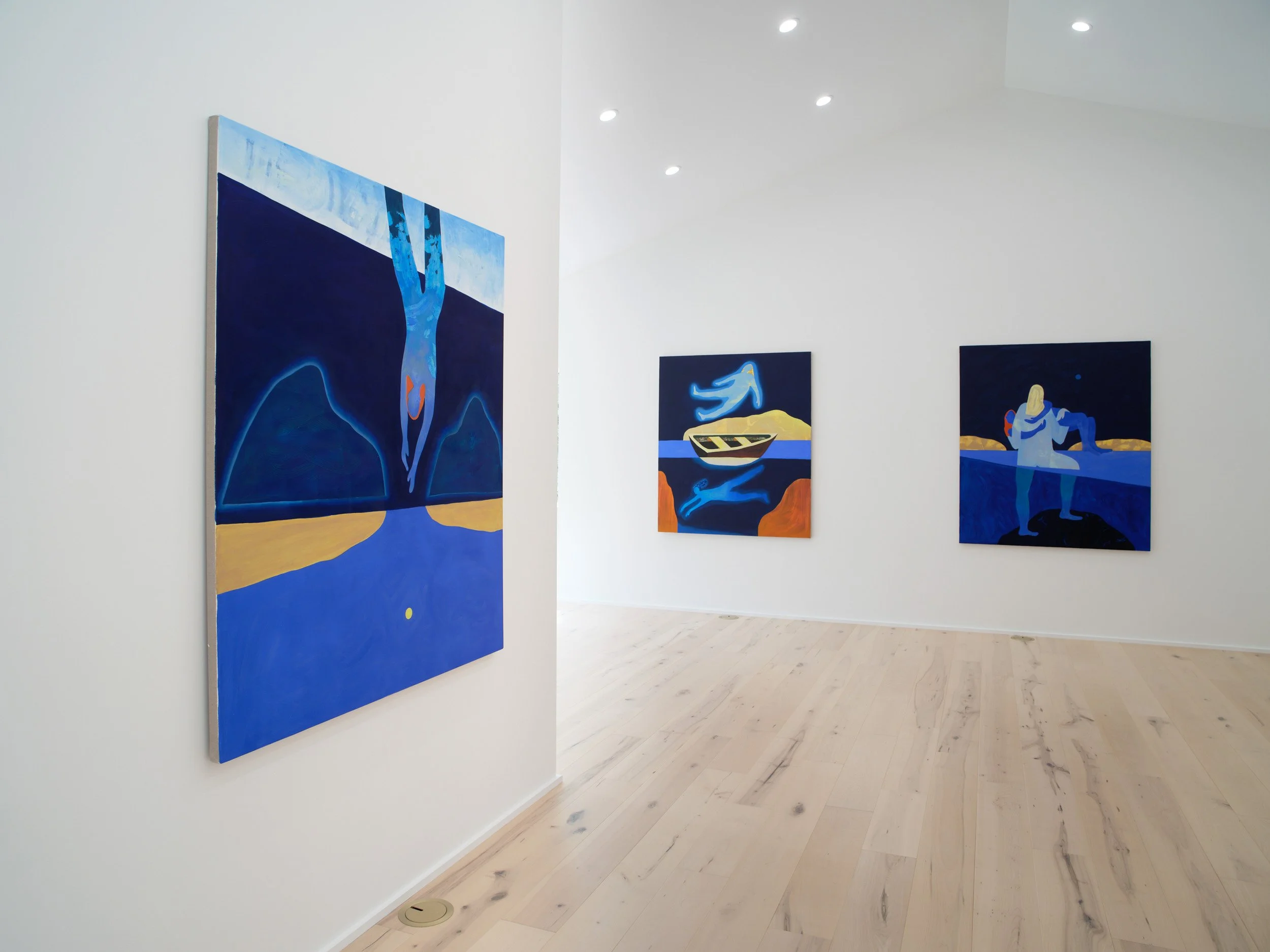 Three abstract paintings with blue, yellow, and orange colors are hung on white gallery walls. The gallery has a light wood floor and ceiling spotlights.