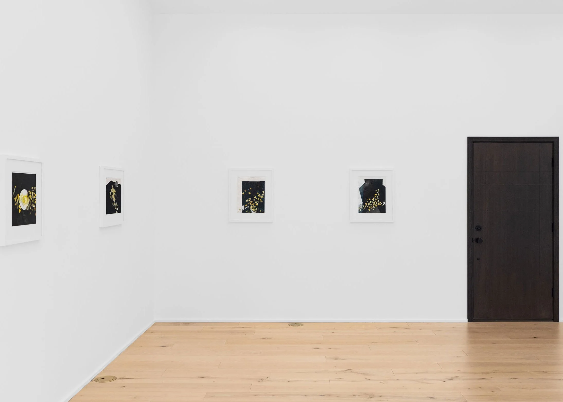 Gallery wall with five artworks featuring geometric and abstract designs, framed in white, with a dark wood door on the right and light wood flooring.