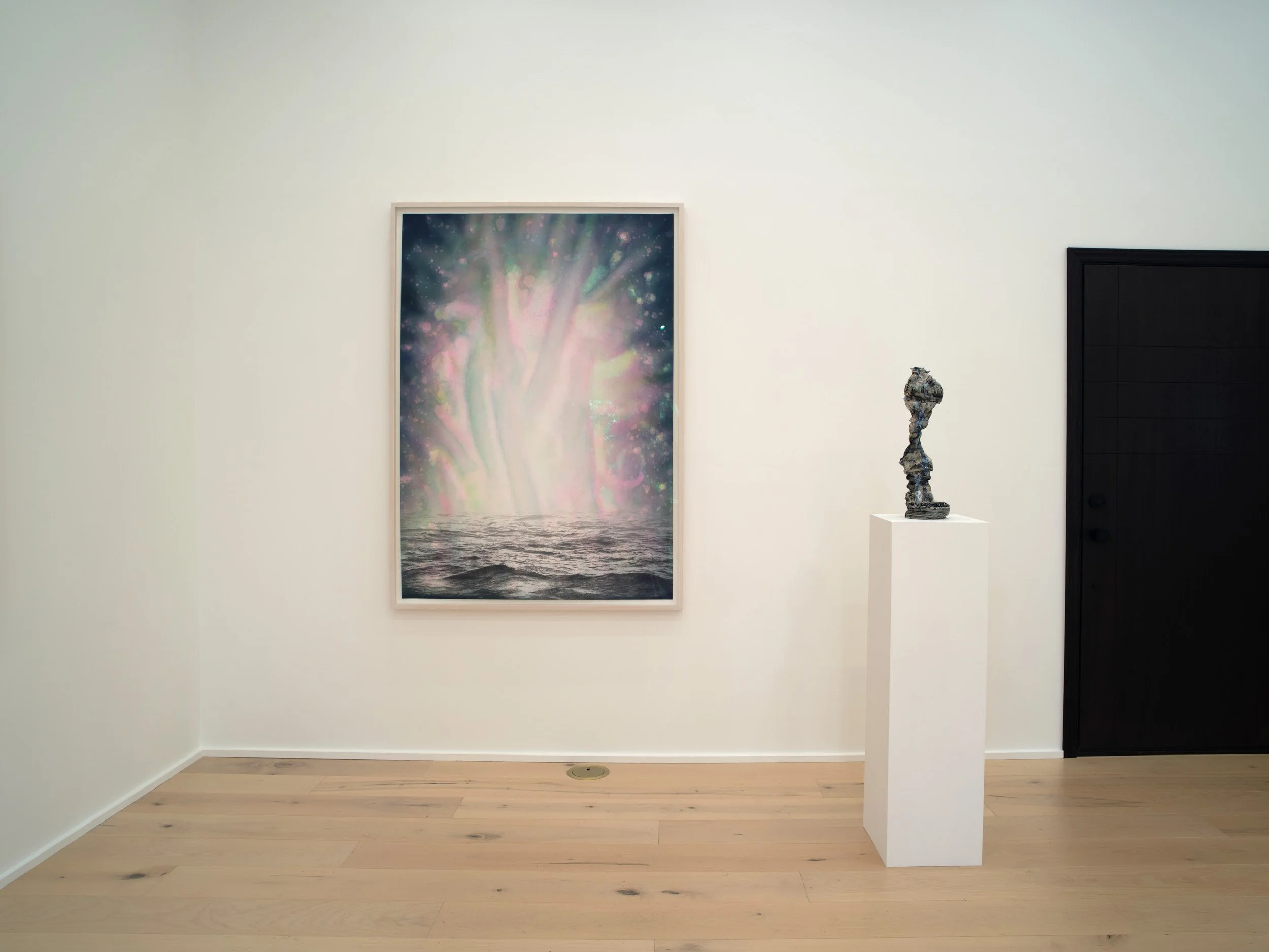 Art gallery with a watercolor painting of a tree on a large framed canvas on white wall, beside a sculpture on a white pedestal, black door on right, light wood floors.