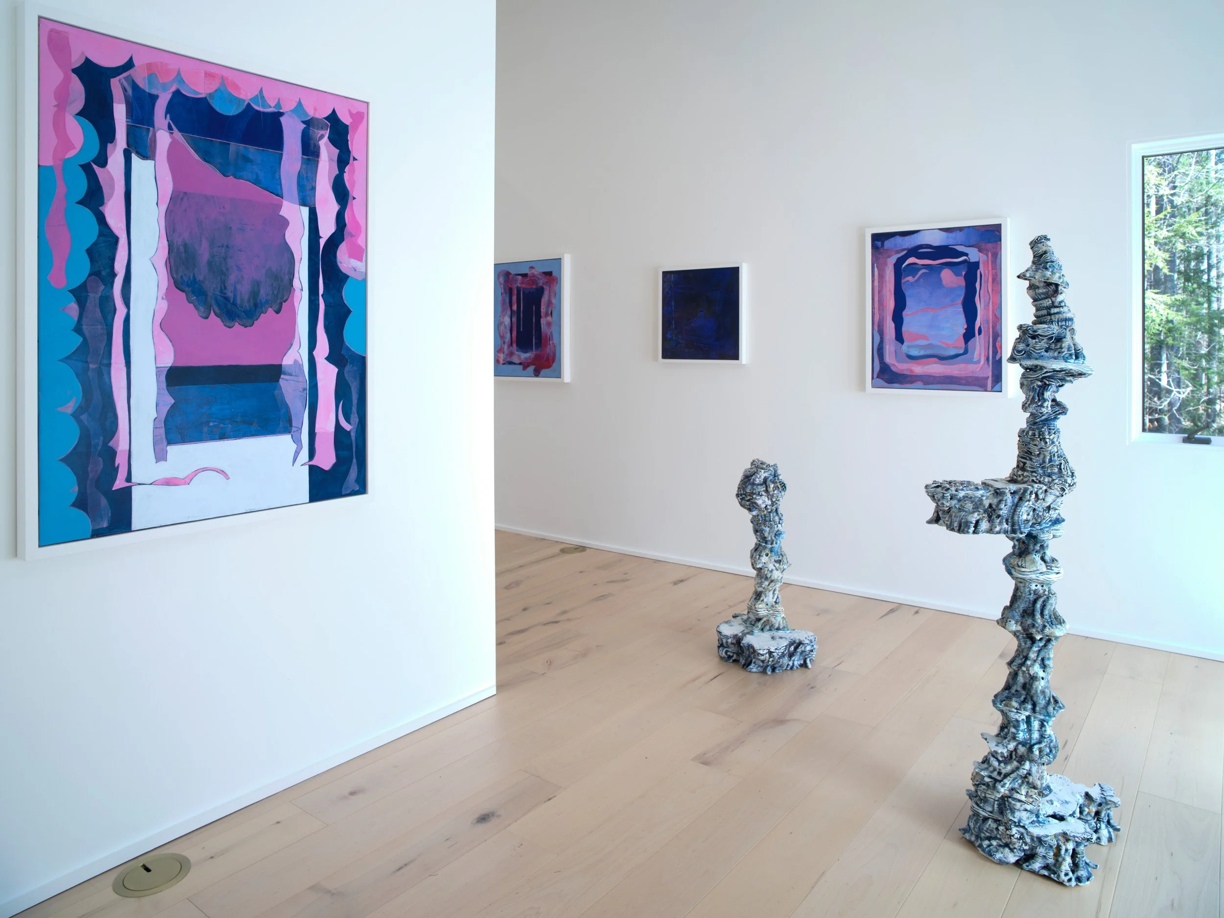 Art gallery displaying abstract paintings in pink, purple, and blue, with ceramic sculptures featuring twisting, textured forms, and a large window showing greenery outside.