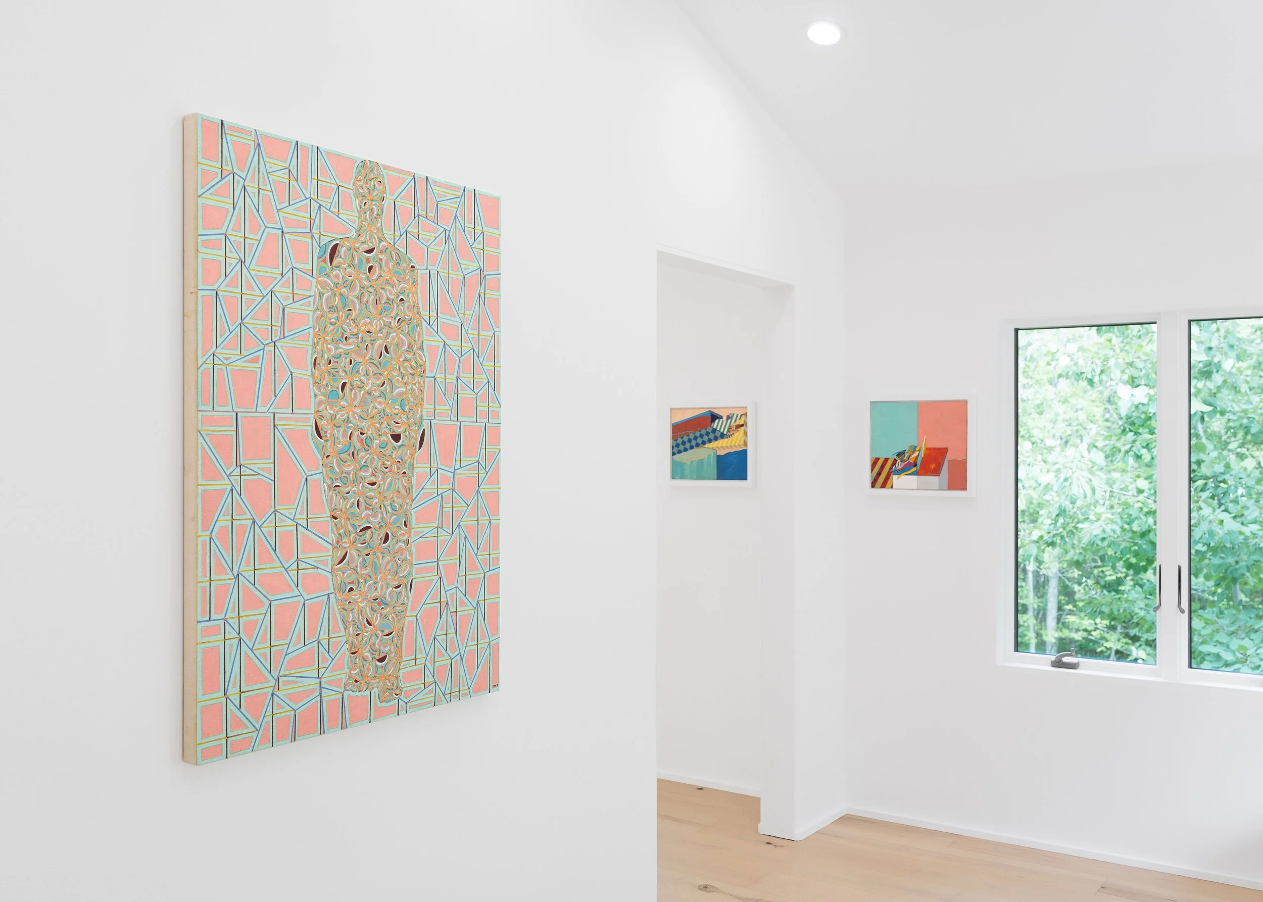 An art gallery with white walls displaying colorful paintings, with a large window showing green foliage outside.