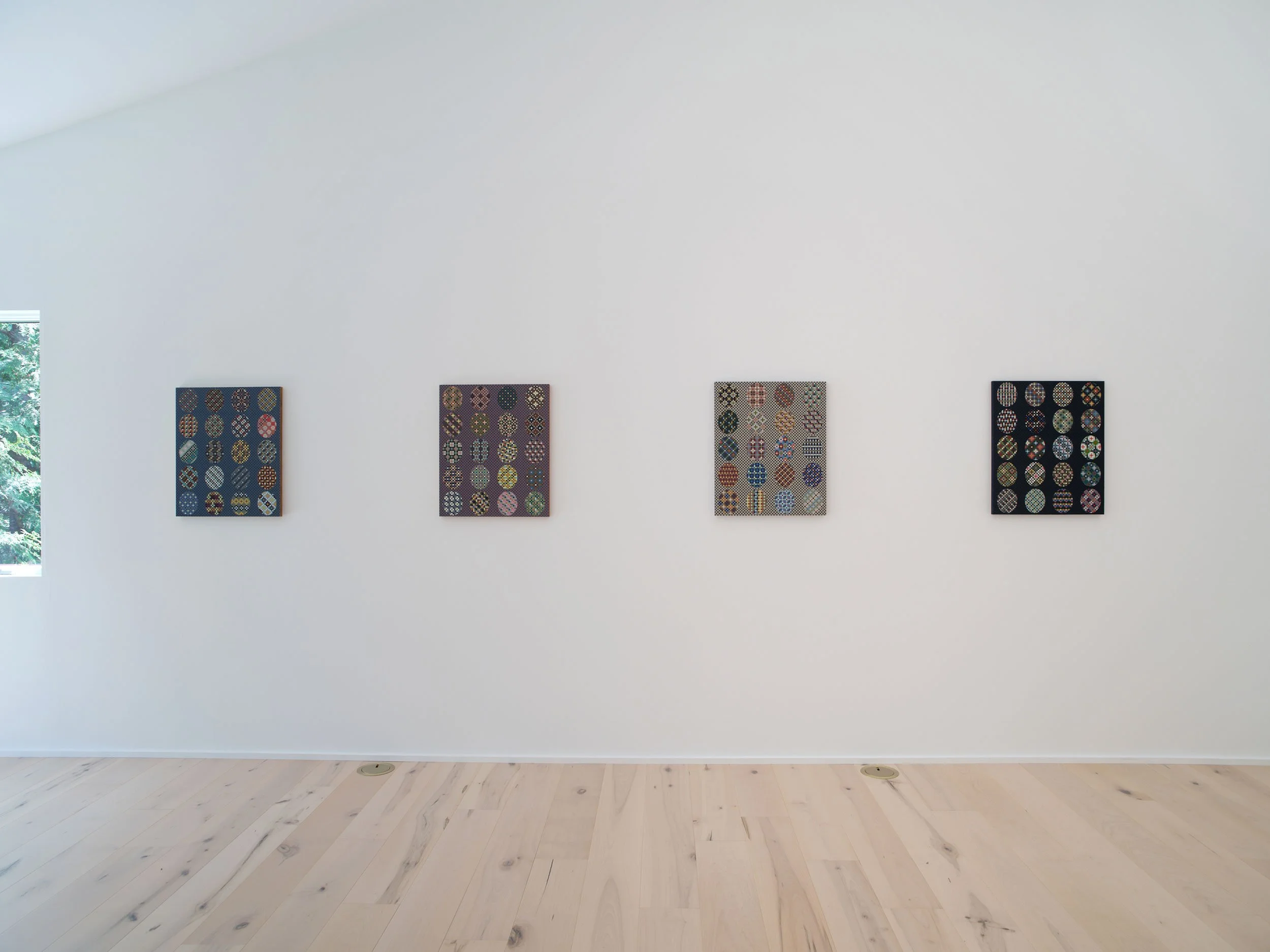 Photo of a white gallery wall with four art pieces, with a window showing greenery on the left.