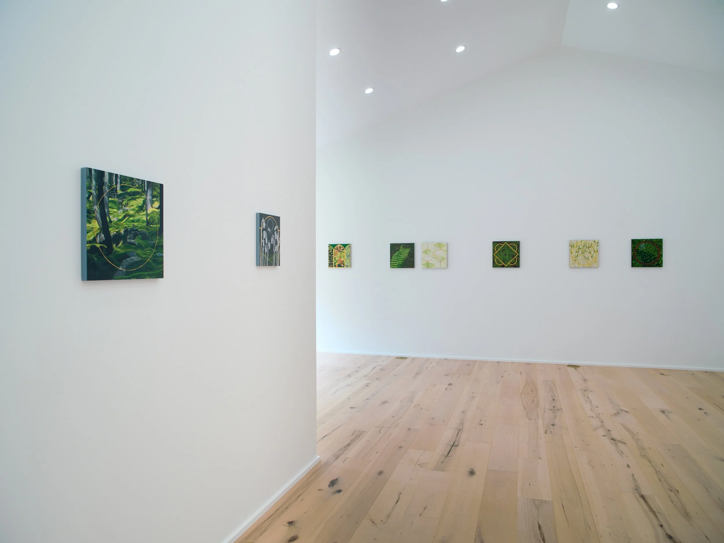 An art gallery wall with a collection of small abstract paintings, with a white wall and wooden floor.