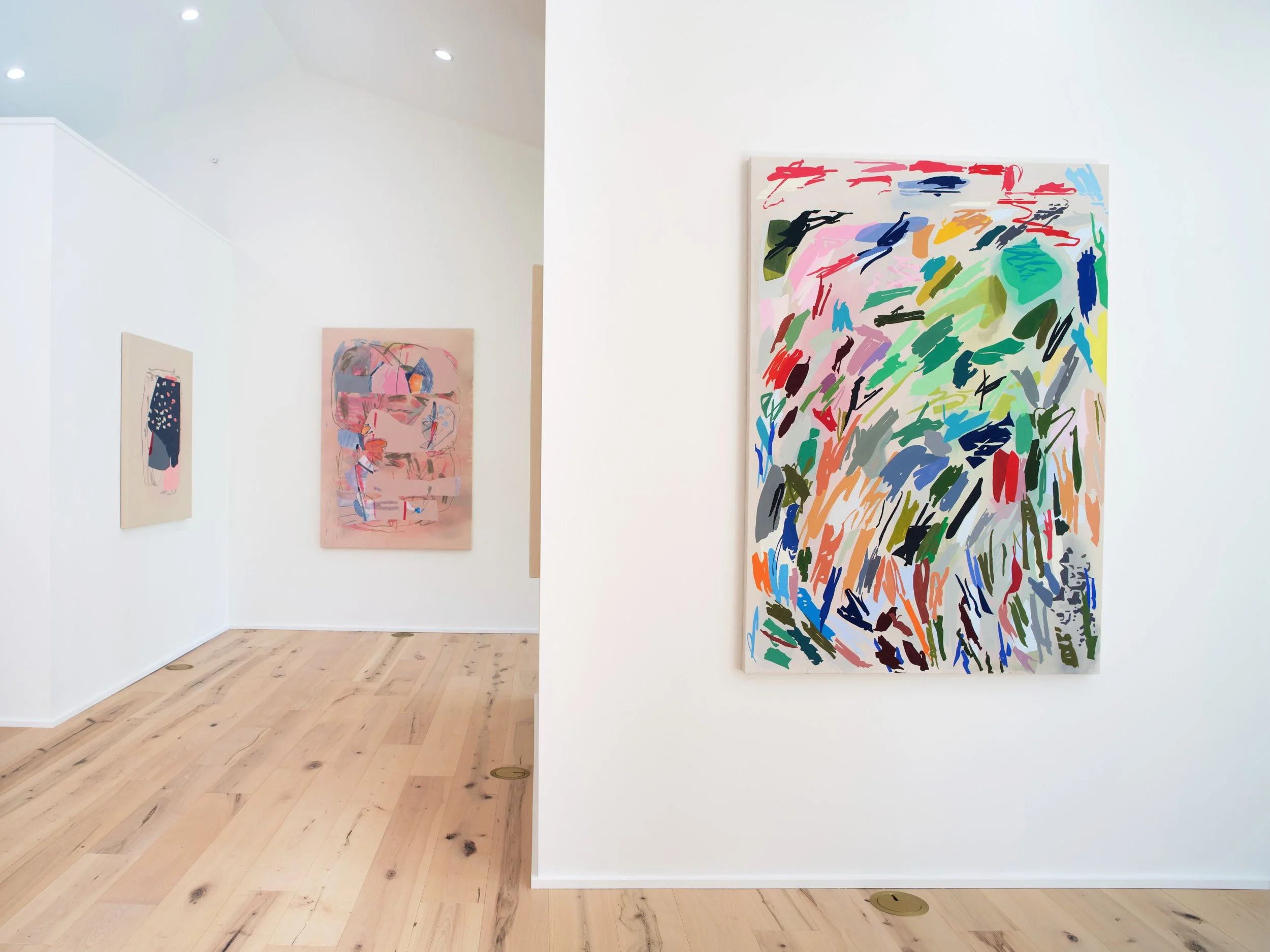 Abstract colorful paintings displayed on white gallery walls with hardwood flooring.