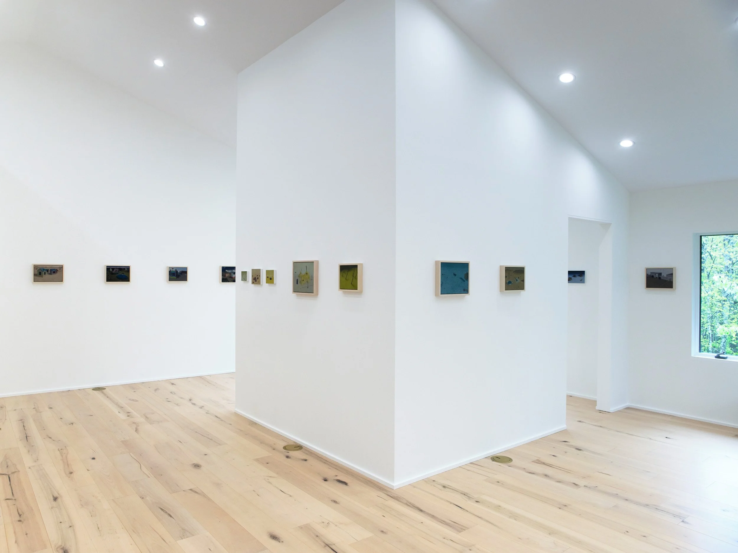 White art gallery walls with small framed artworks and wooden floors illuminated by ceiling lights.