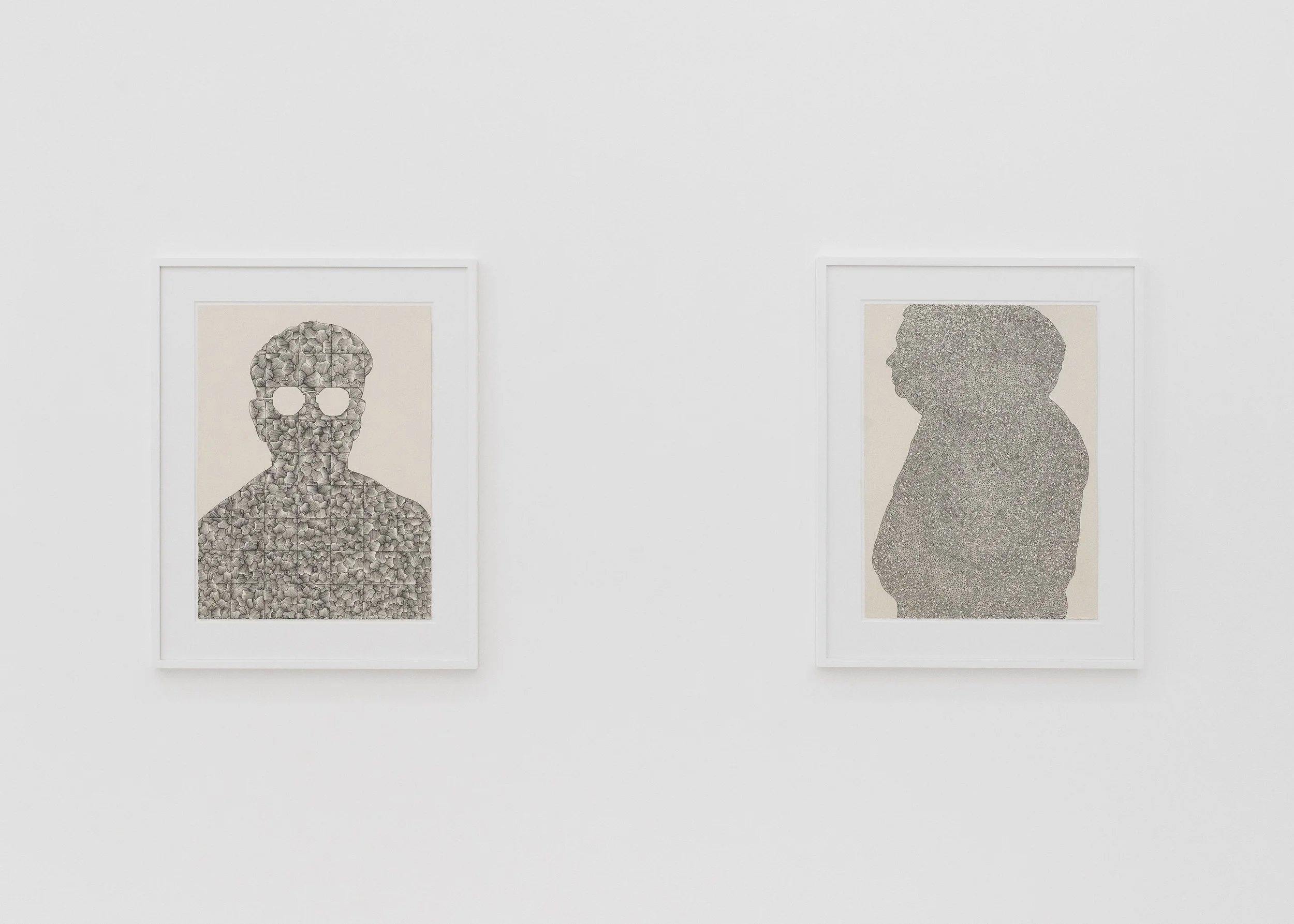Two framed art pieces on a white gallery wall. The left features a human skull made of small, textured elements, and the right depicts a silhouette of a person's profile filled with a pattern of tiny dots.