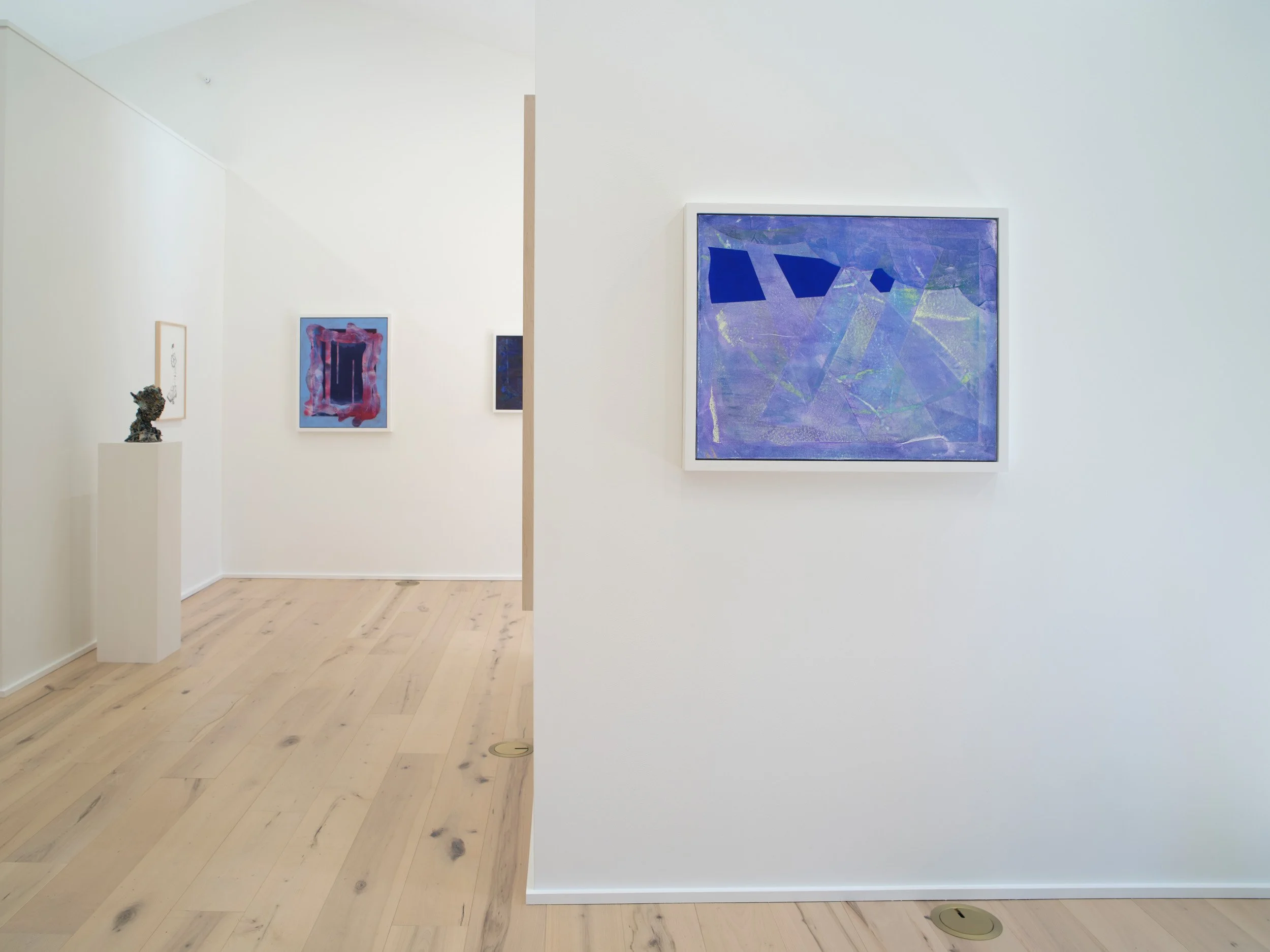 An art gallery with white walls and light wood floors displaying abstract paintings and sculptures.