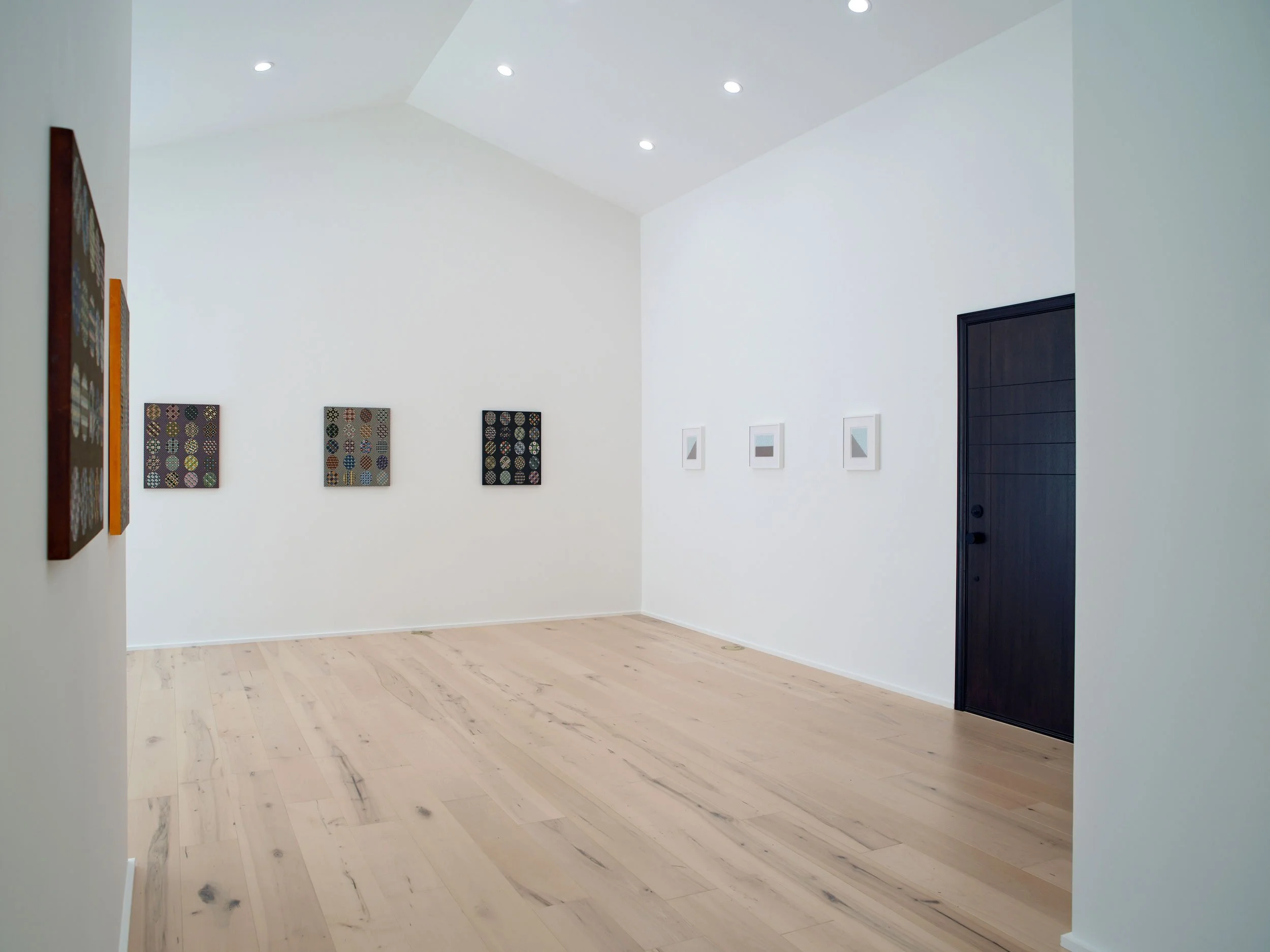 Empty room with white walls, light-colored wooden floor, small paintings on the walls, black door, and ceiling lights.