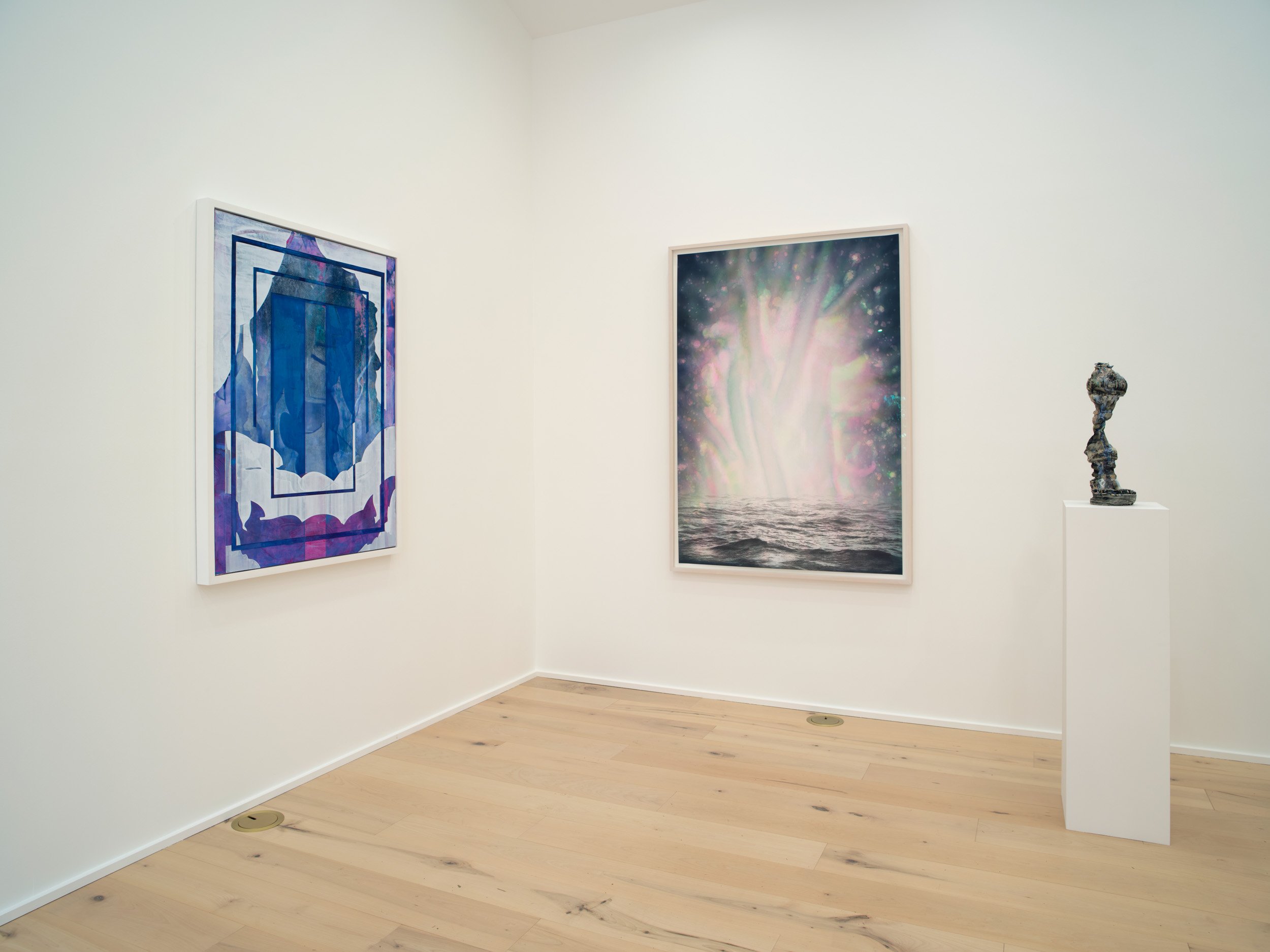 Gallery wall with two framed abstract paintings, one on the left with shades of blue and purple, and one on the right with a colorful cosmic or nebula theme, and a sculpture on a pedestal on the right side.